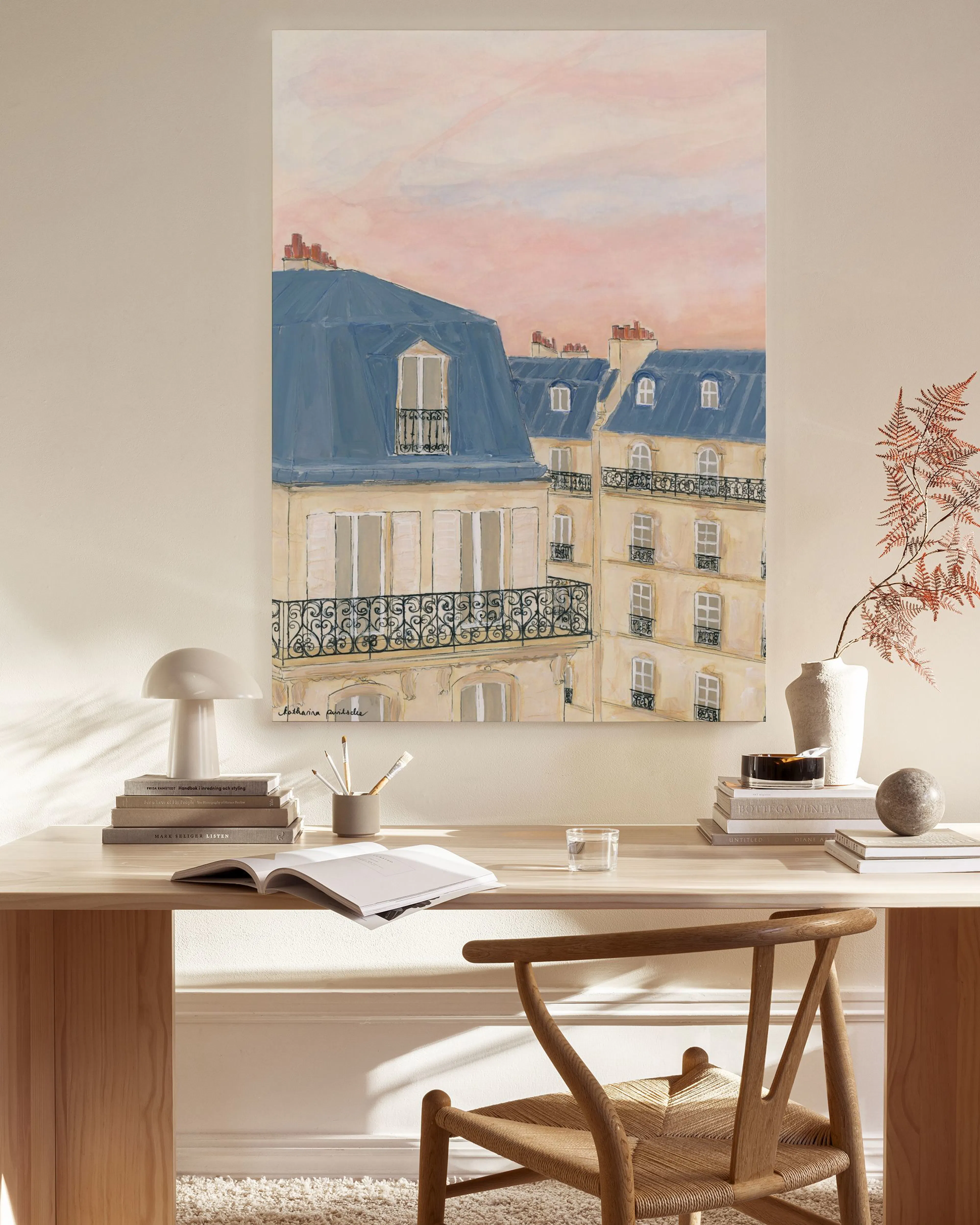 Leinwandbild mit pastellfarbenen Pariser Dächern unter rosafarbenem Himmel, über einem Holzregal im Wohnzimmer.