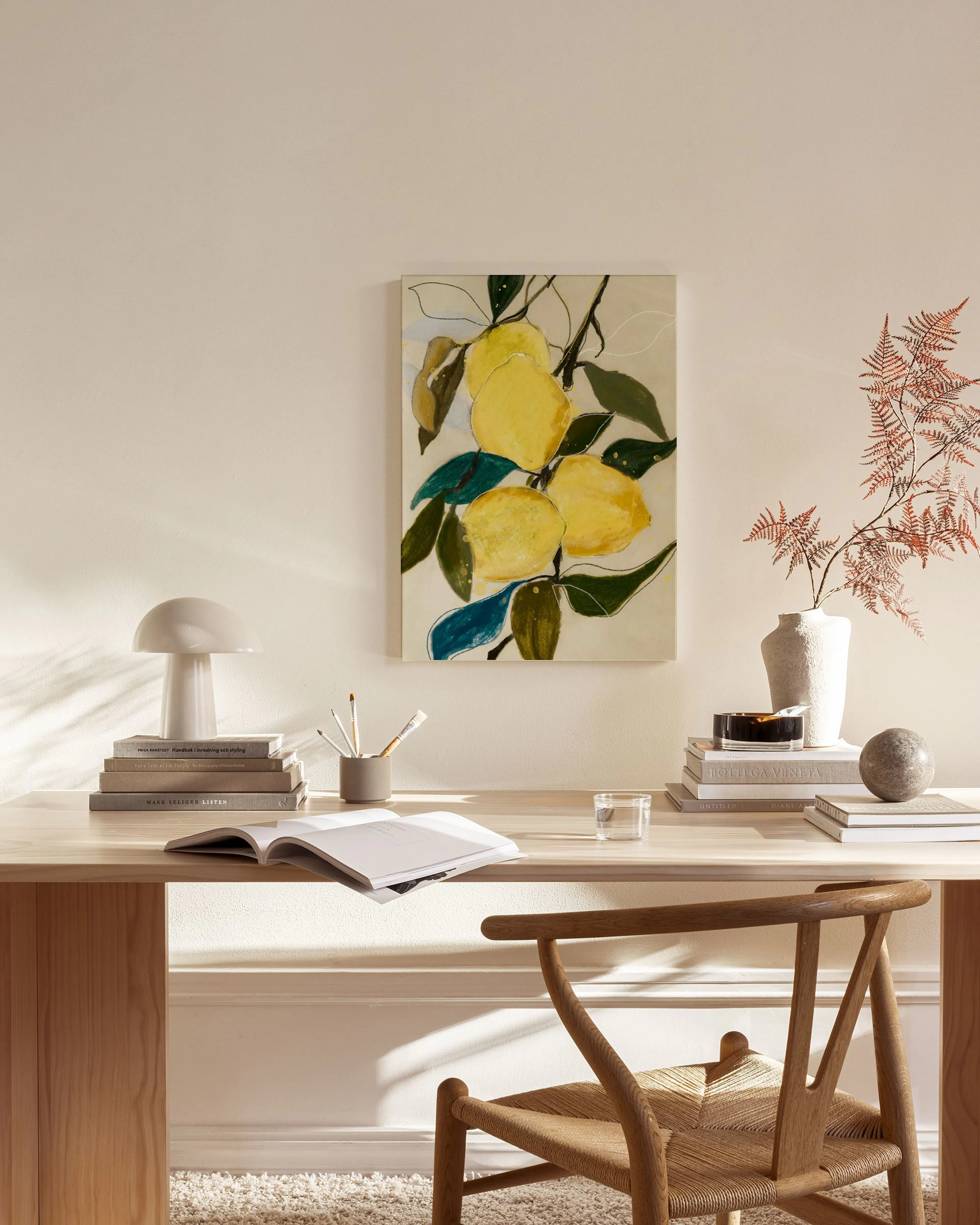 Toile murale de citrons jaunes et feuilles vertes, accrochée dans un salon moderne avec fauteuil en bois et table basse en verre