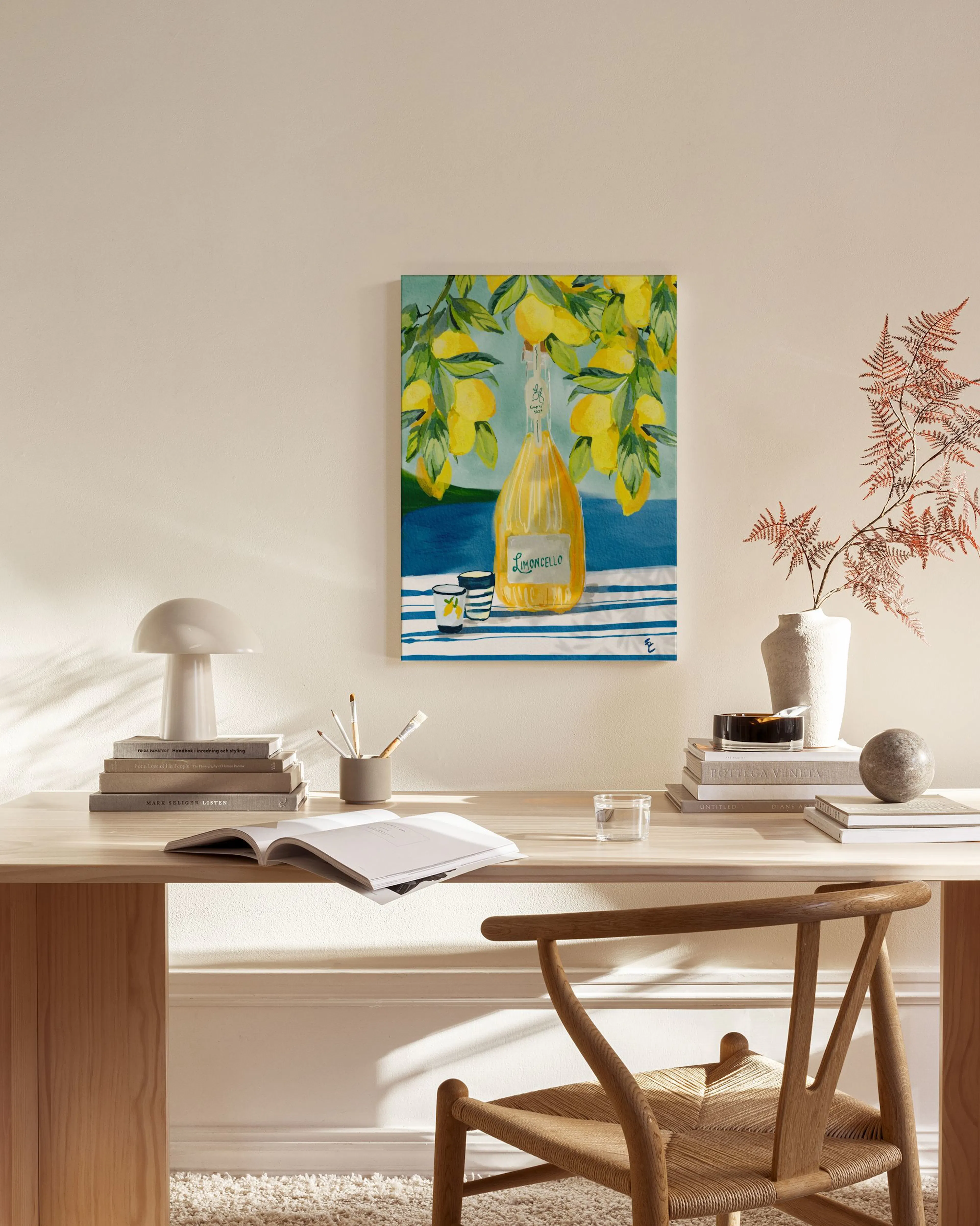 A Limoncello bottle and two glasses on a striped blue and white tablecloth with lemons, hanging in a modern living room.