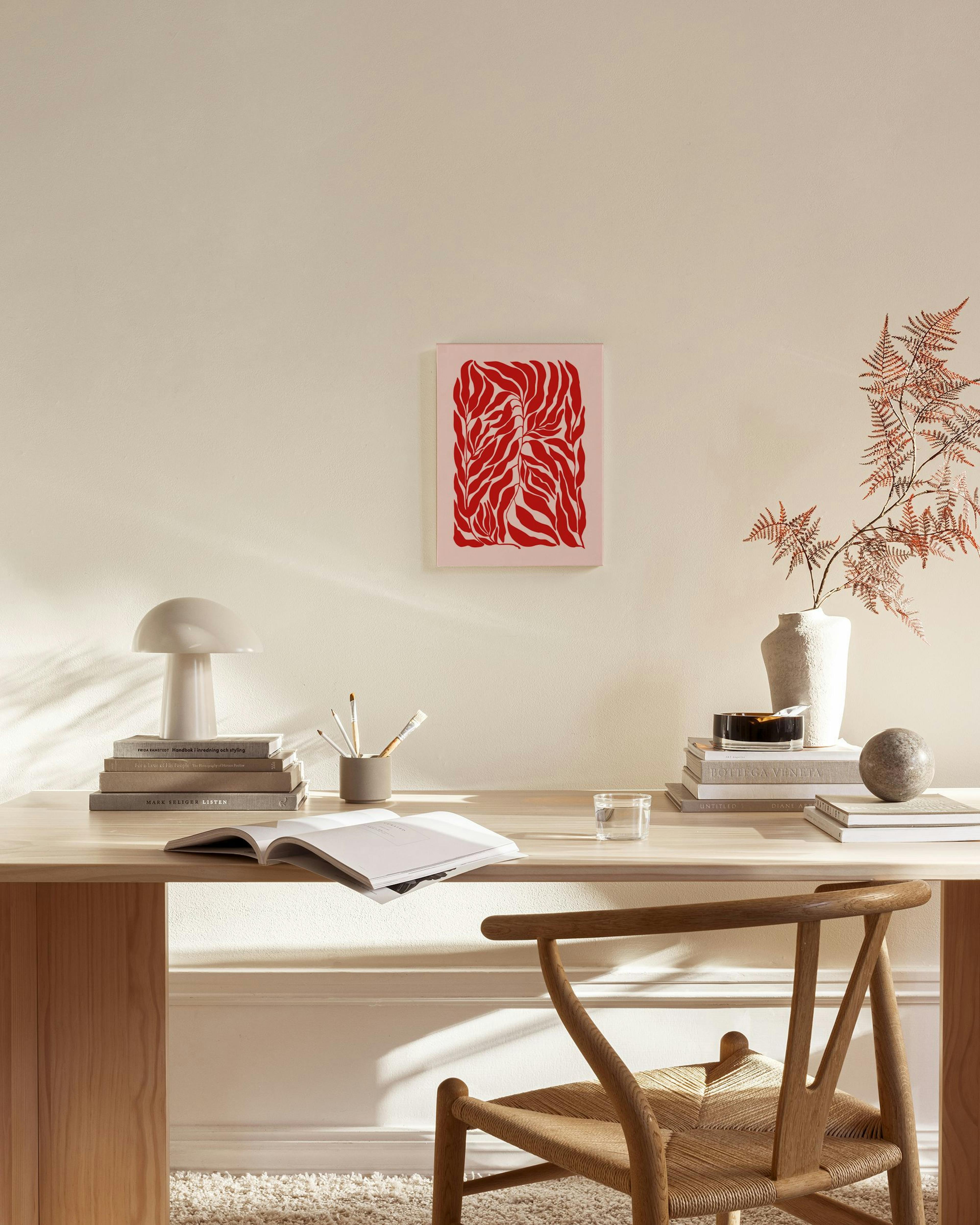 Toile murale rouge vif à motifs de feuilles sur fond rose pâle, suspendue dans un salon moderne au-dessus dun banc en bois clair