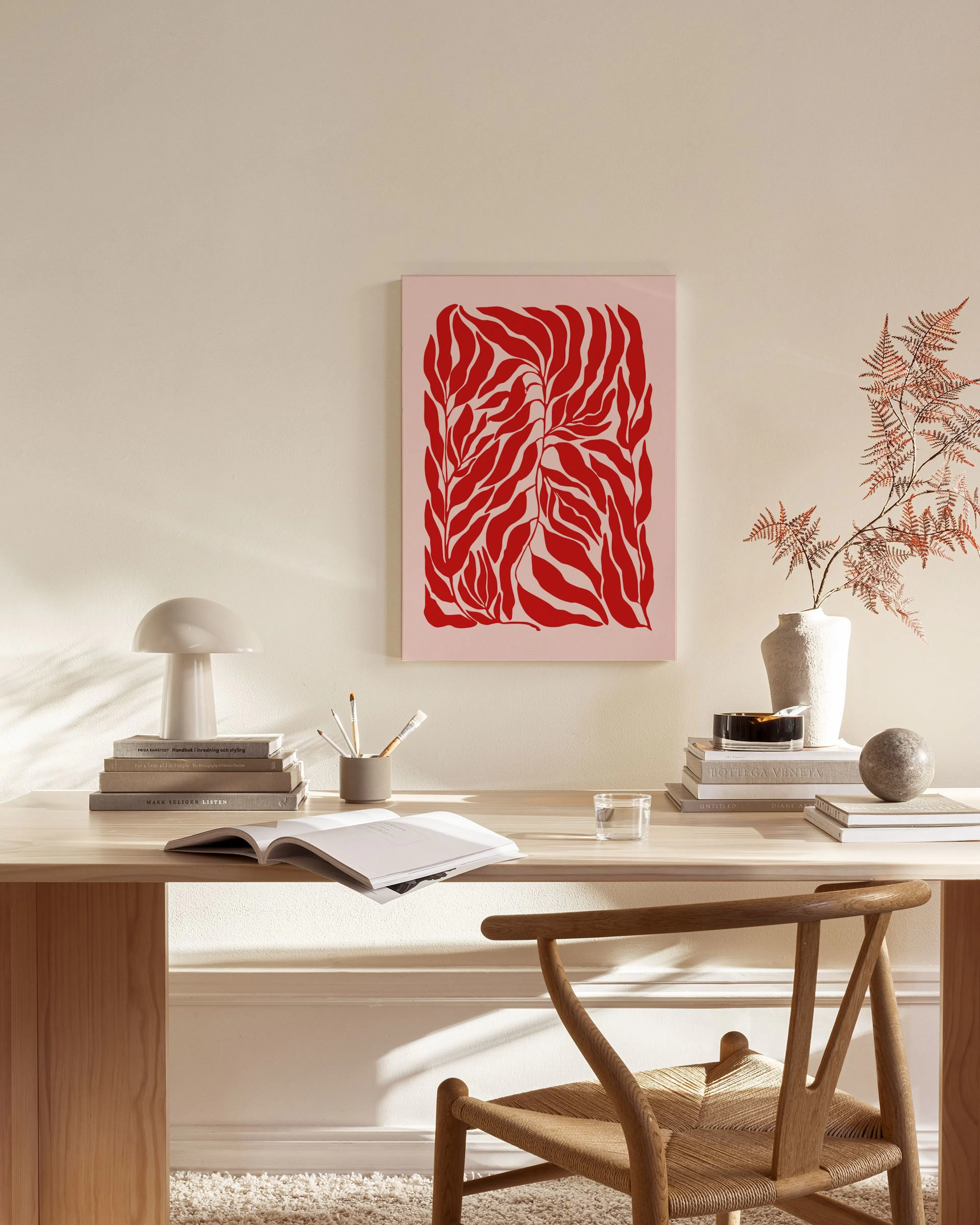 Canvas met rode bladeren op een lichte roze achtergrond, hangend in een moderne woonkamer boven een dressoir.