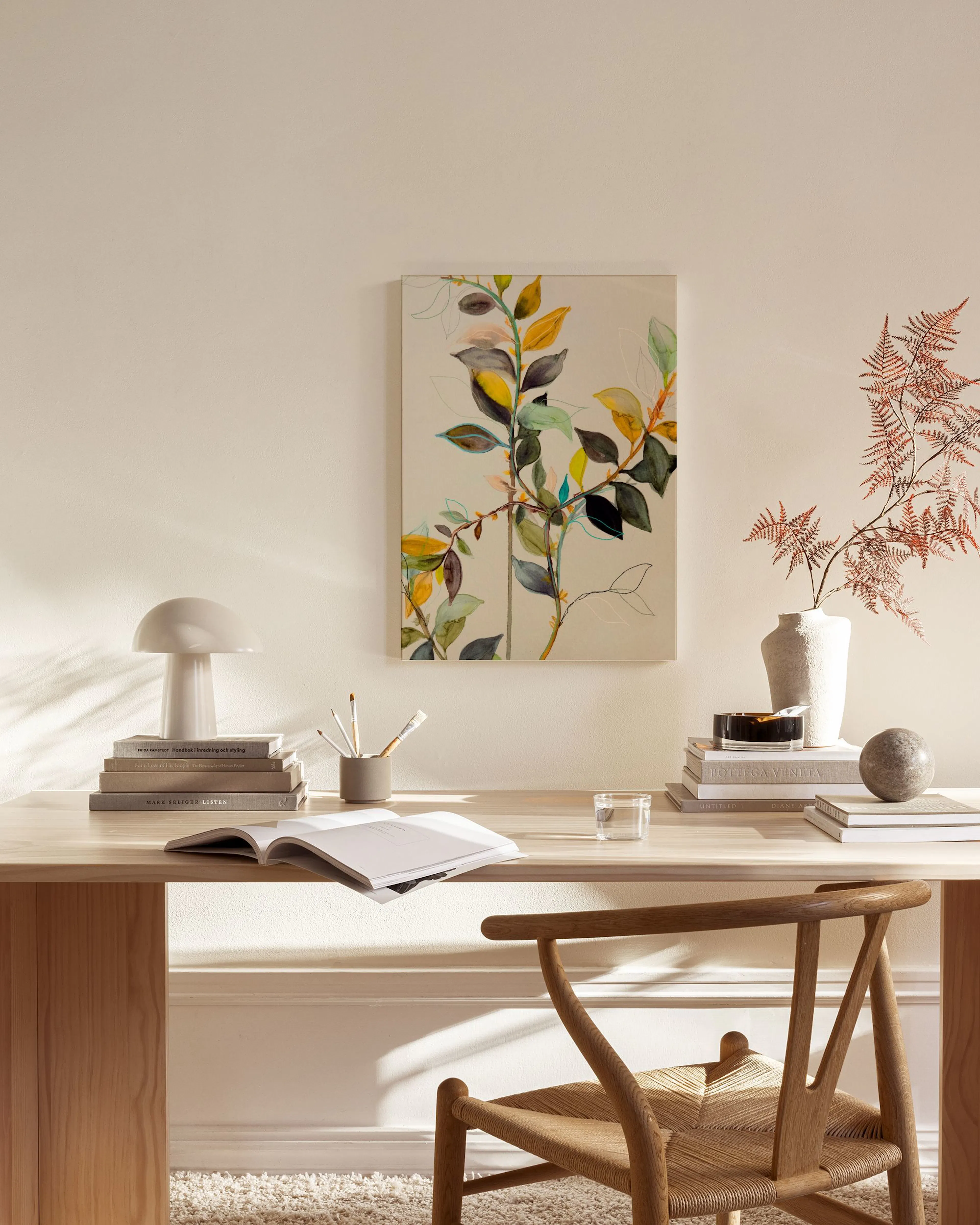 Canvas met herfstbladeren in geel, groen en donkerbruin, hangend in een neutrale woonkamer boven een dressoir.