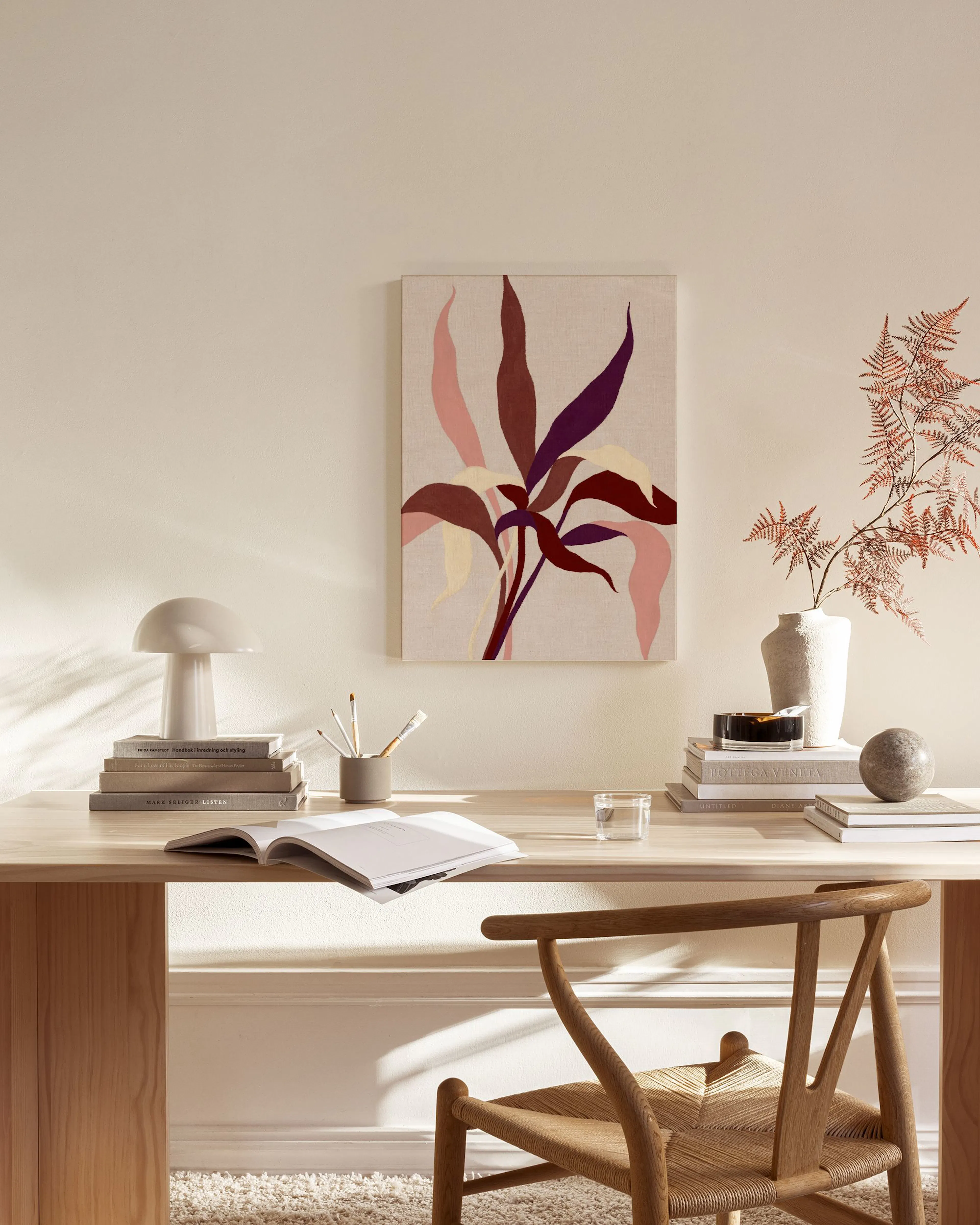 Botanical canvas print featuring maroon, plum, and pink leaves, hanging in a neutral-toned living room with a timber chair and g