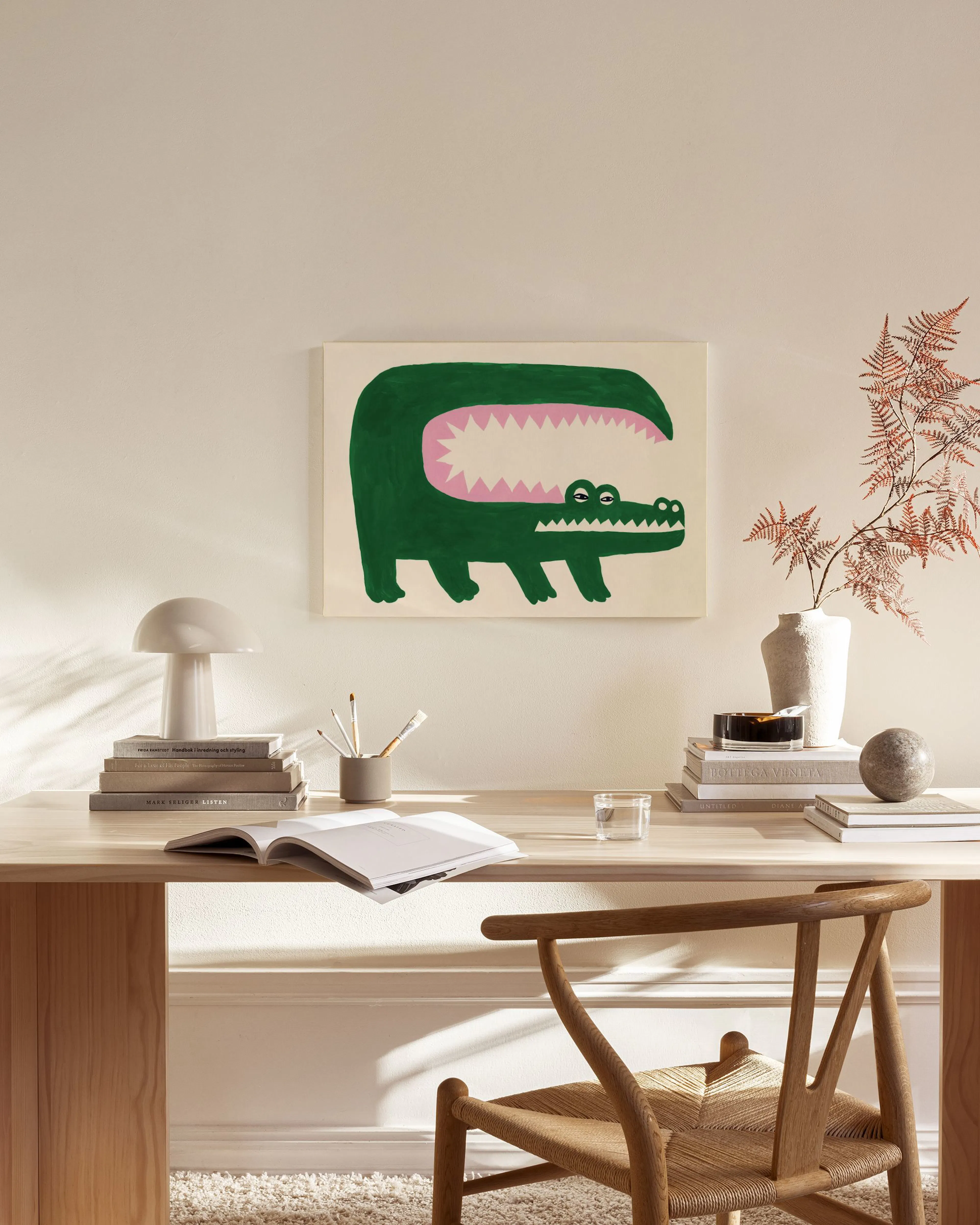 Canvastavla med grön krokodil med rosa mun, hängandes i ett ljust vardagsrum över en bänk.