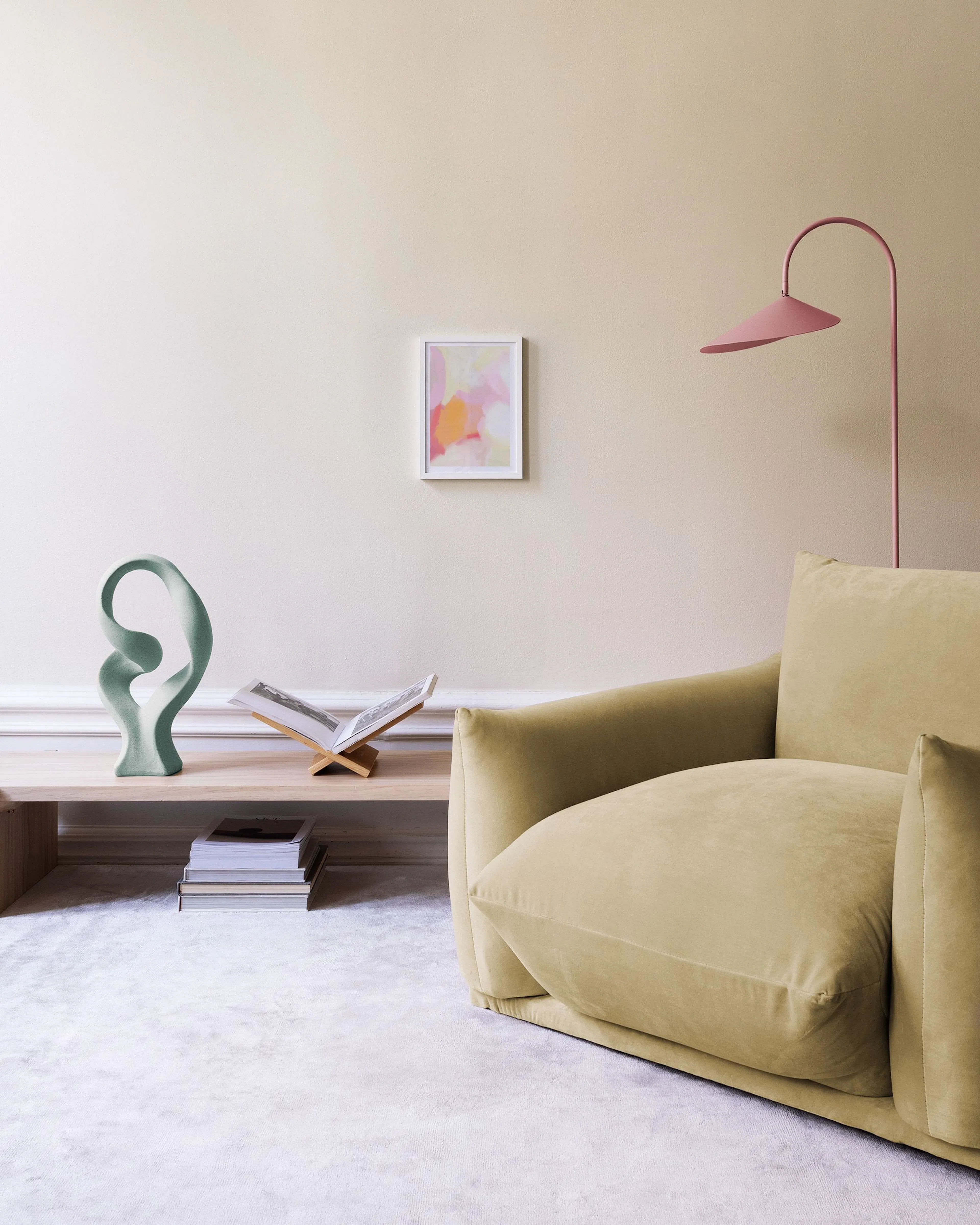 Poster mit abstrakten Formen in Rosa, Orange und Gelb, hängend über einem Holztisch mit Buch und Blumenvase.