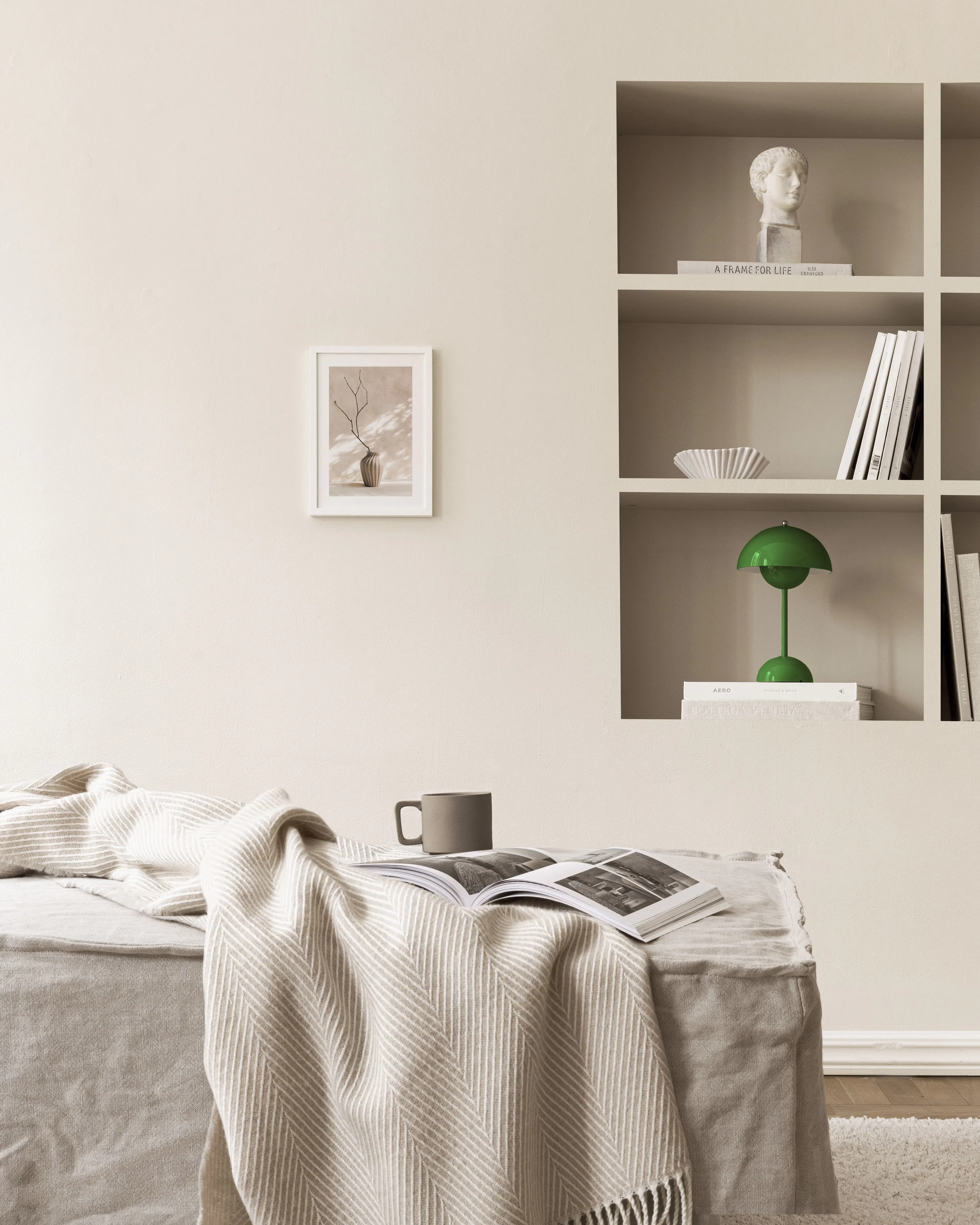 Juliste vaaleanbeigellä taustalla olevasta beigestä maljakosta, jossa on kuiva oksa. Juliste on ripustettu beigelle seinälle, ja