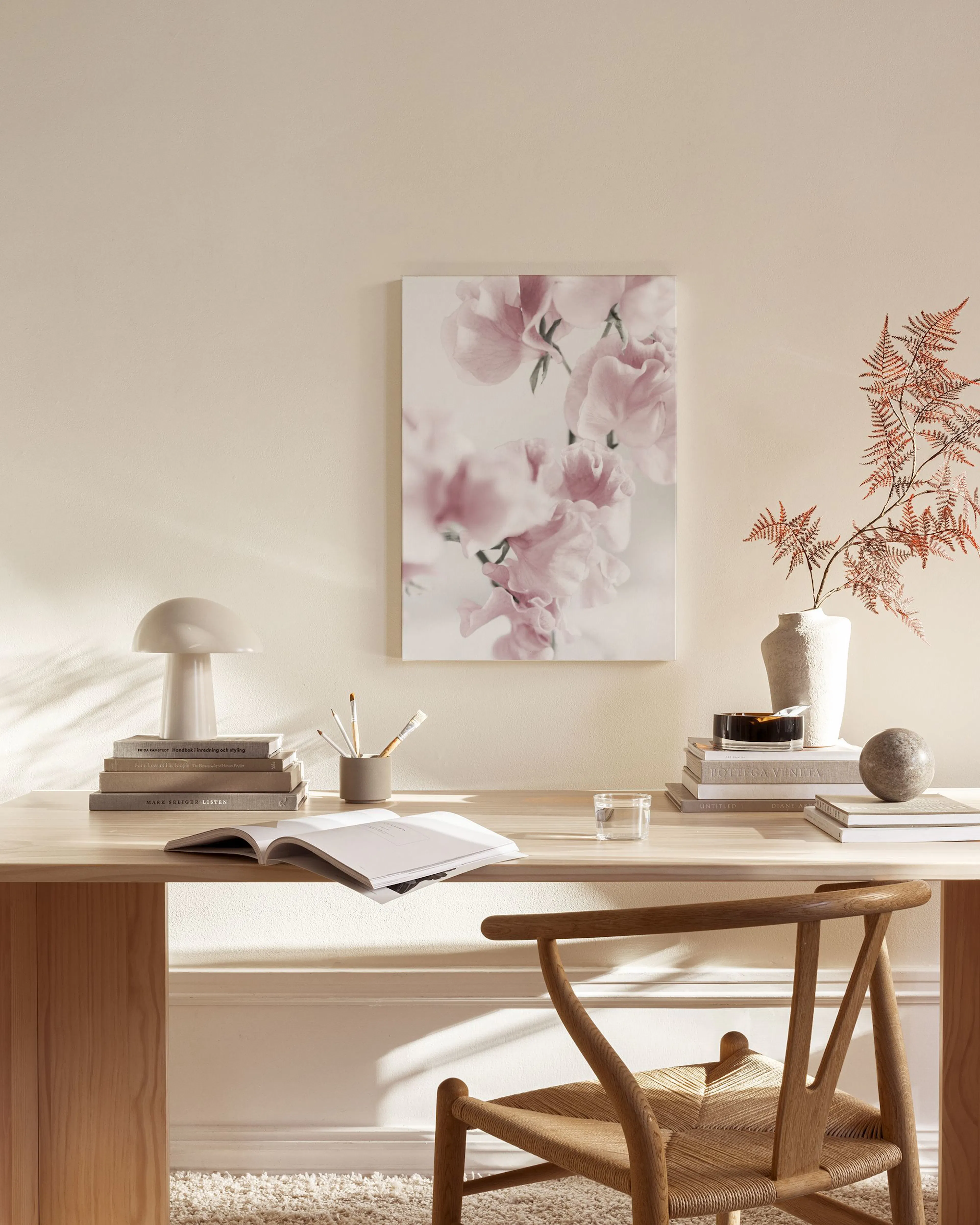 Lienzo de flores rosadas suaves colgando sobre un mueble de madera, con una lámpara y una silla de madera en una sala.