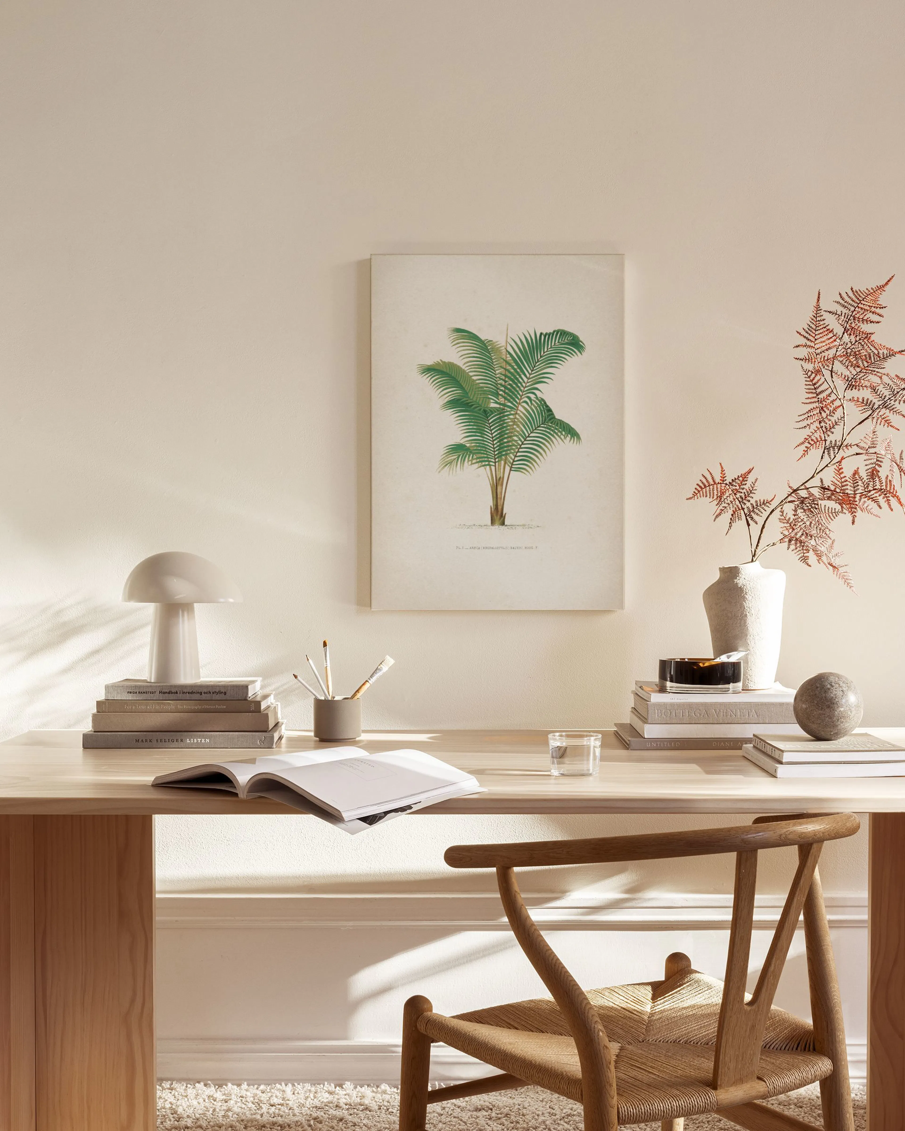 A botanical canvas print of a green palm tree, hanging above a wooden console table in a minimalist living room.