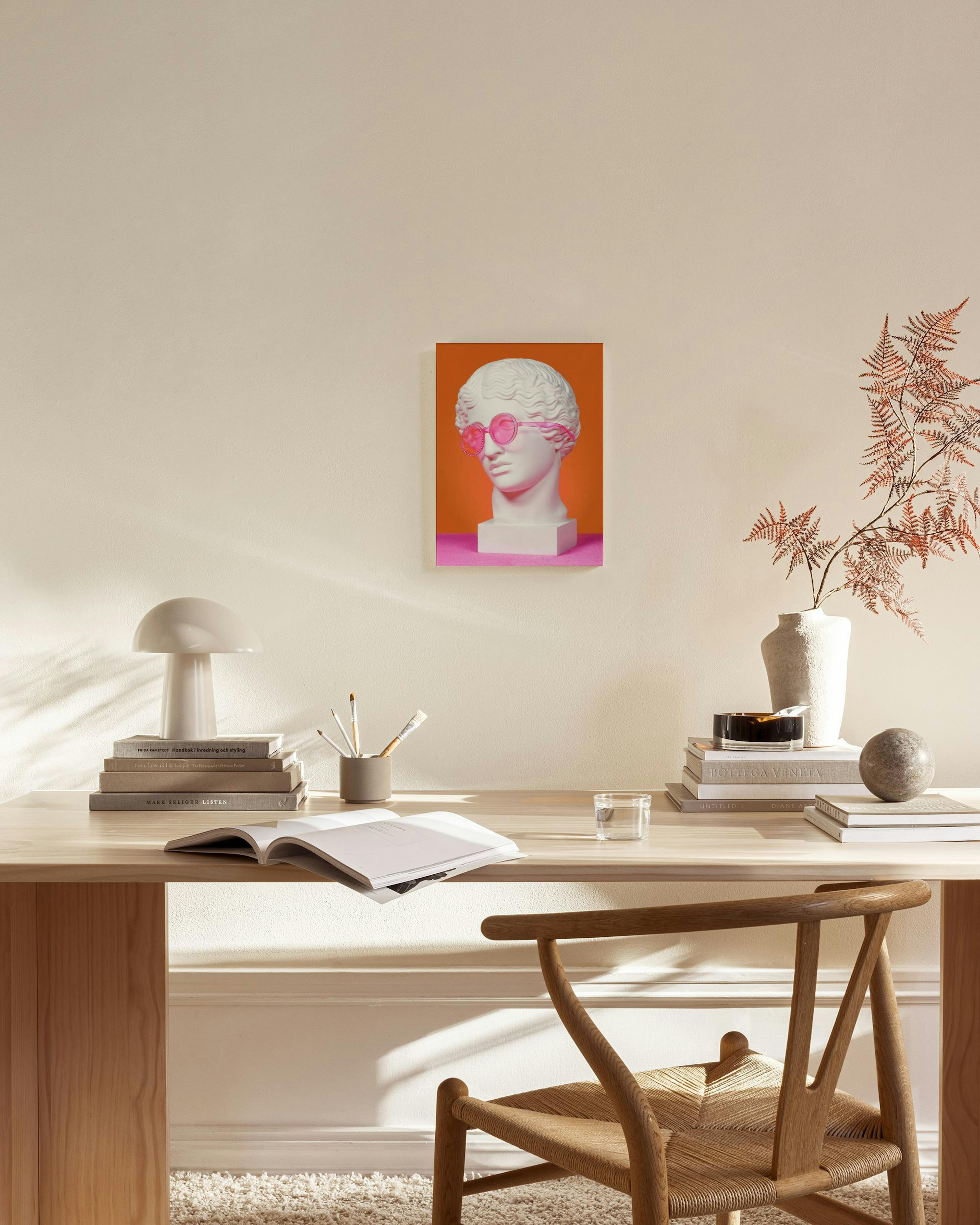 A canvas print of a white classical bust wearing pink sunglasses, on a vibrant orange and pink background, displayed in a modern