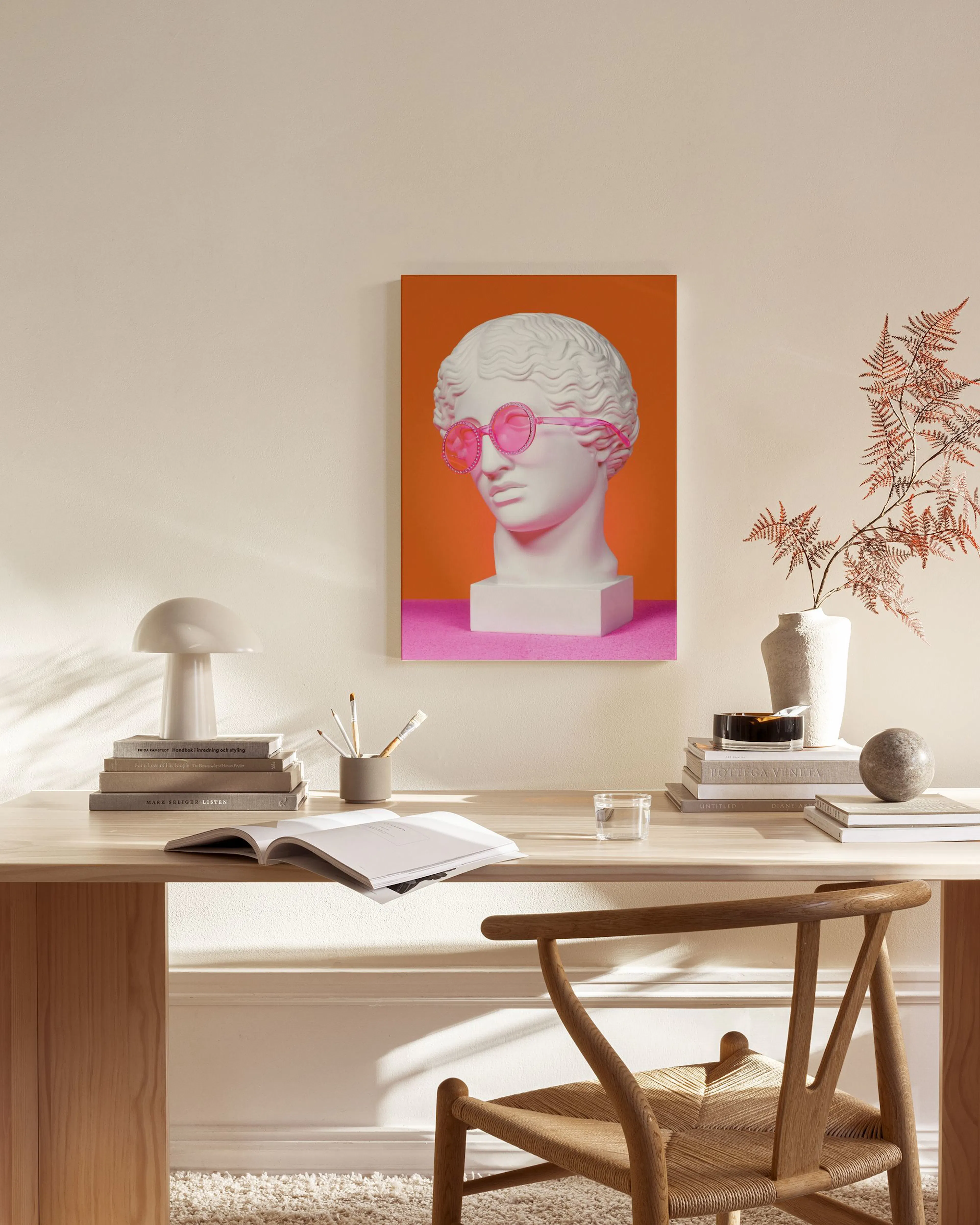 A pop art print of a white classical bust wearing pink sunglasses, on an orange and magenta background, hanging in a modern livi