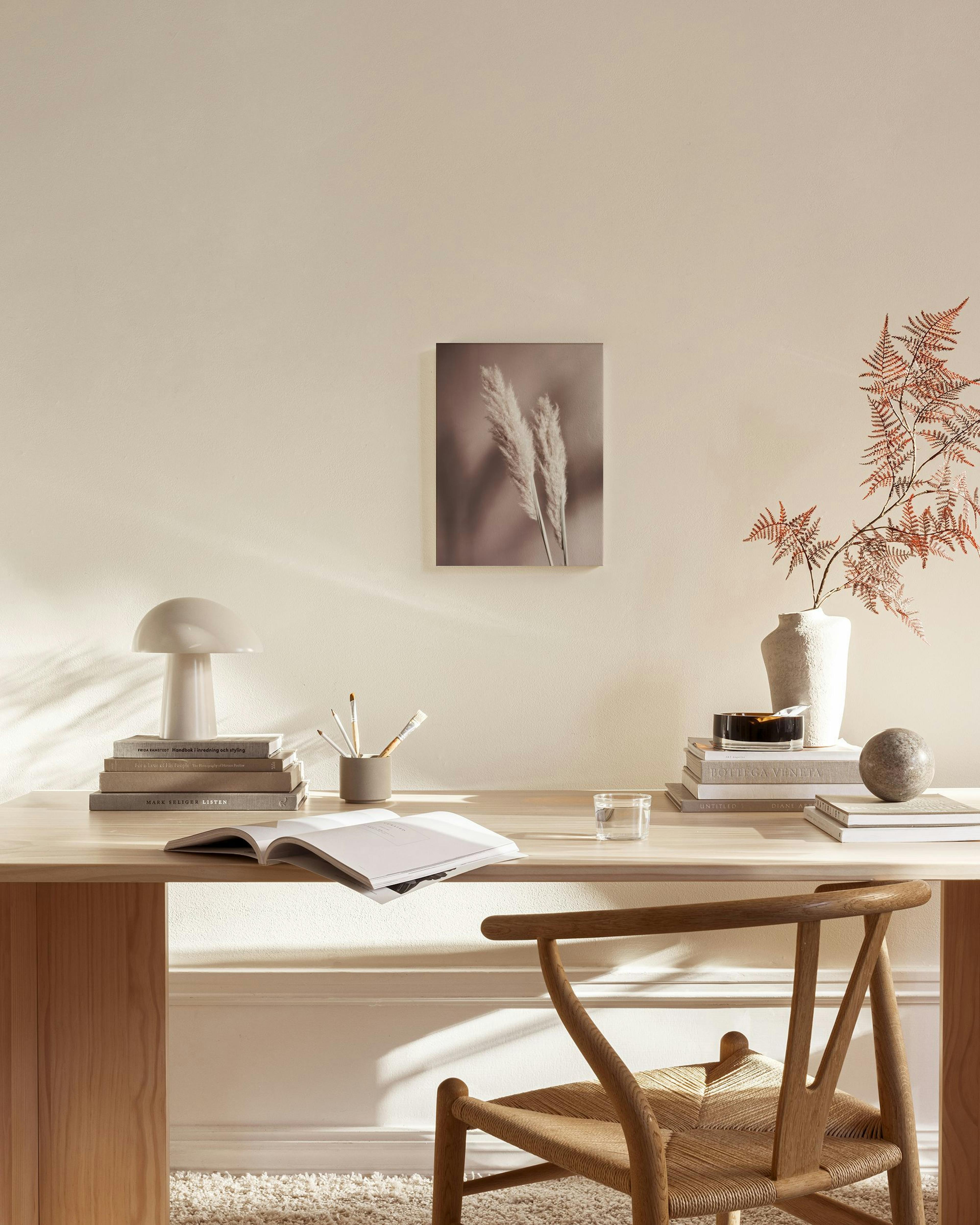 Canvas met twee pluizige pampasgrassen op een roze-bruine achtergrond, hangend boven een houten dressoir in een lichte woonkamer