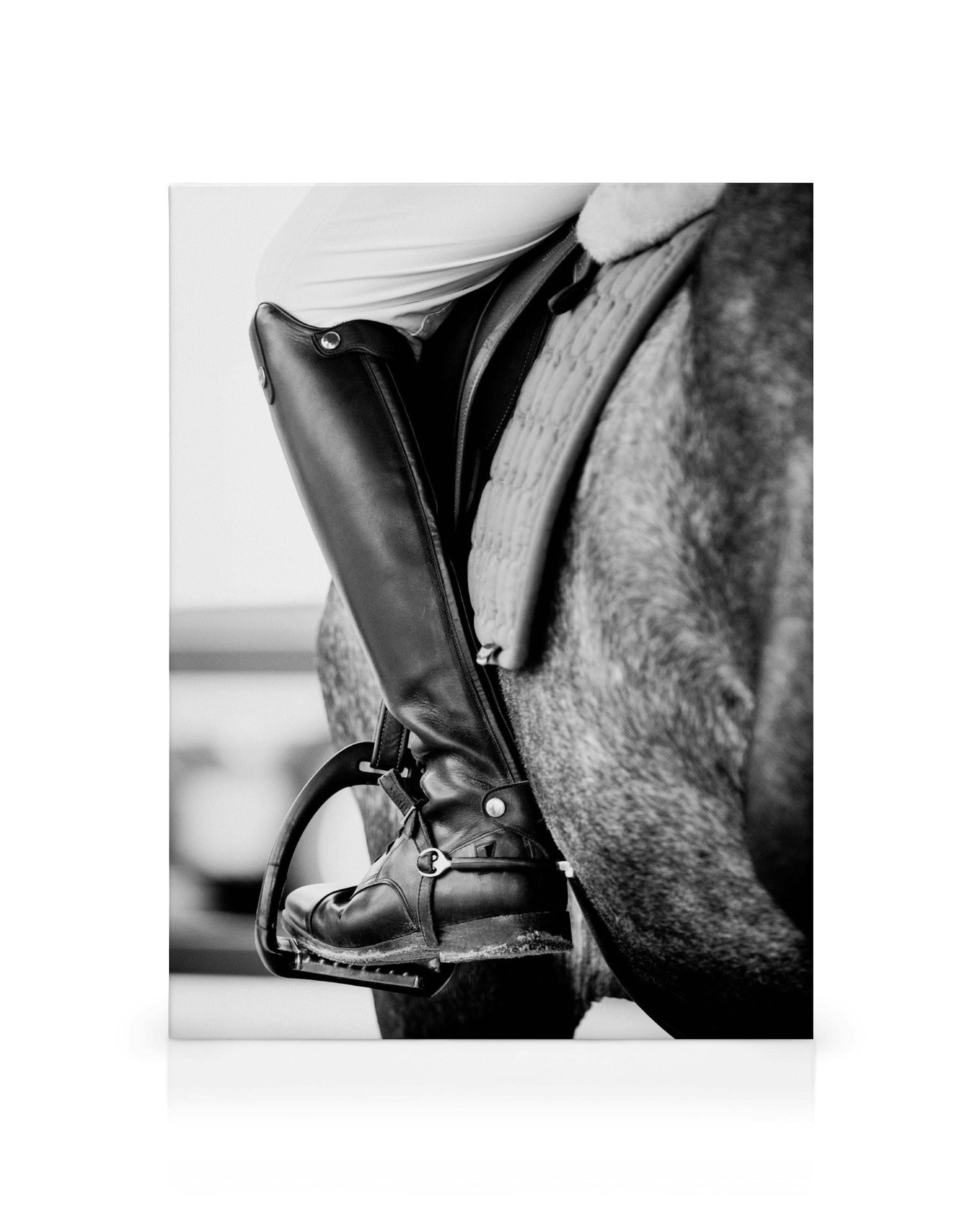 Black and white horse riding canvas print featuring a riders leg in a shiny black boot and stirrup.
