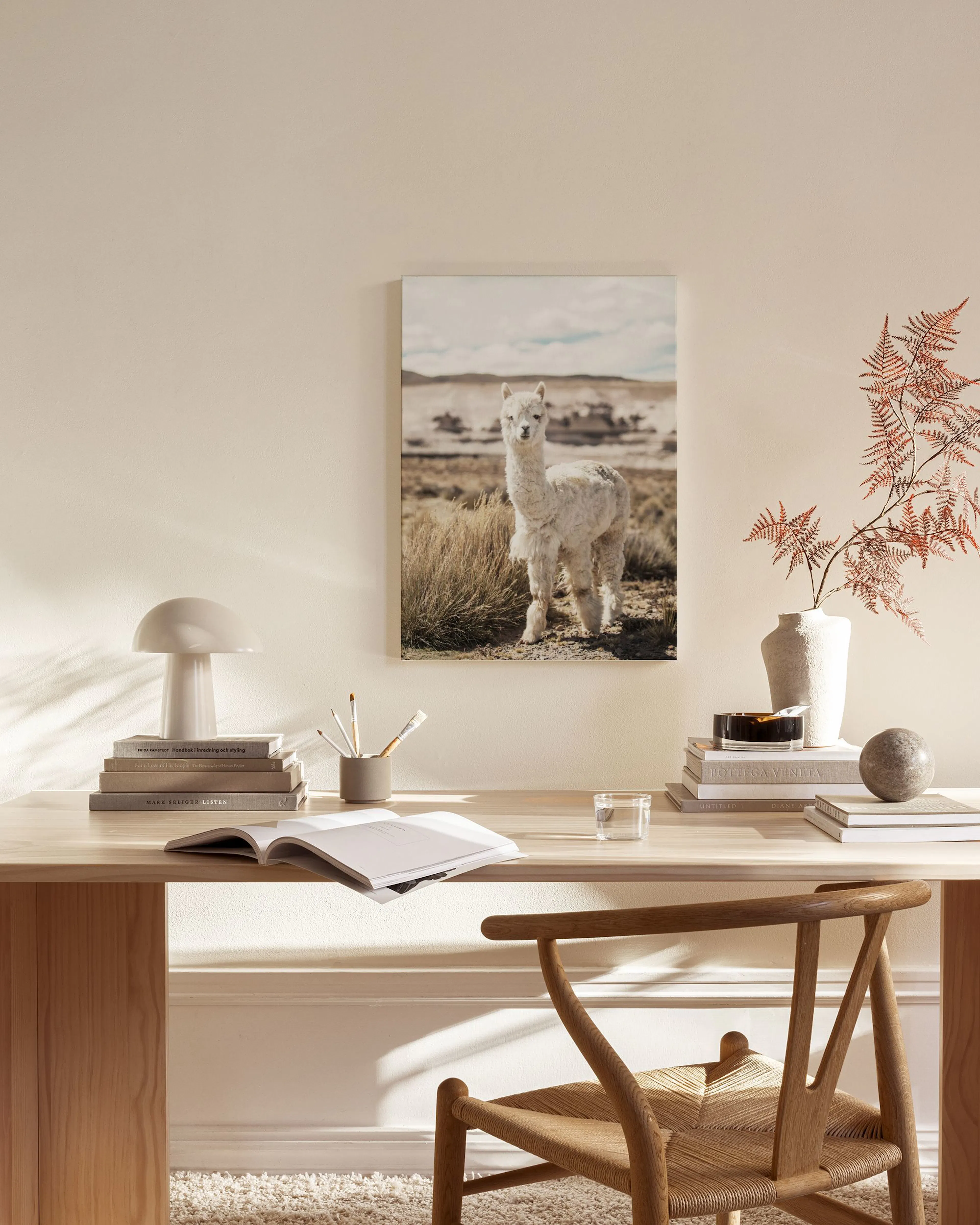 Lienzo de una alpaca blanca de pie en un campo de hierba, colgado en una sala de estar moderna con muebles de madera.