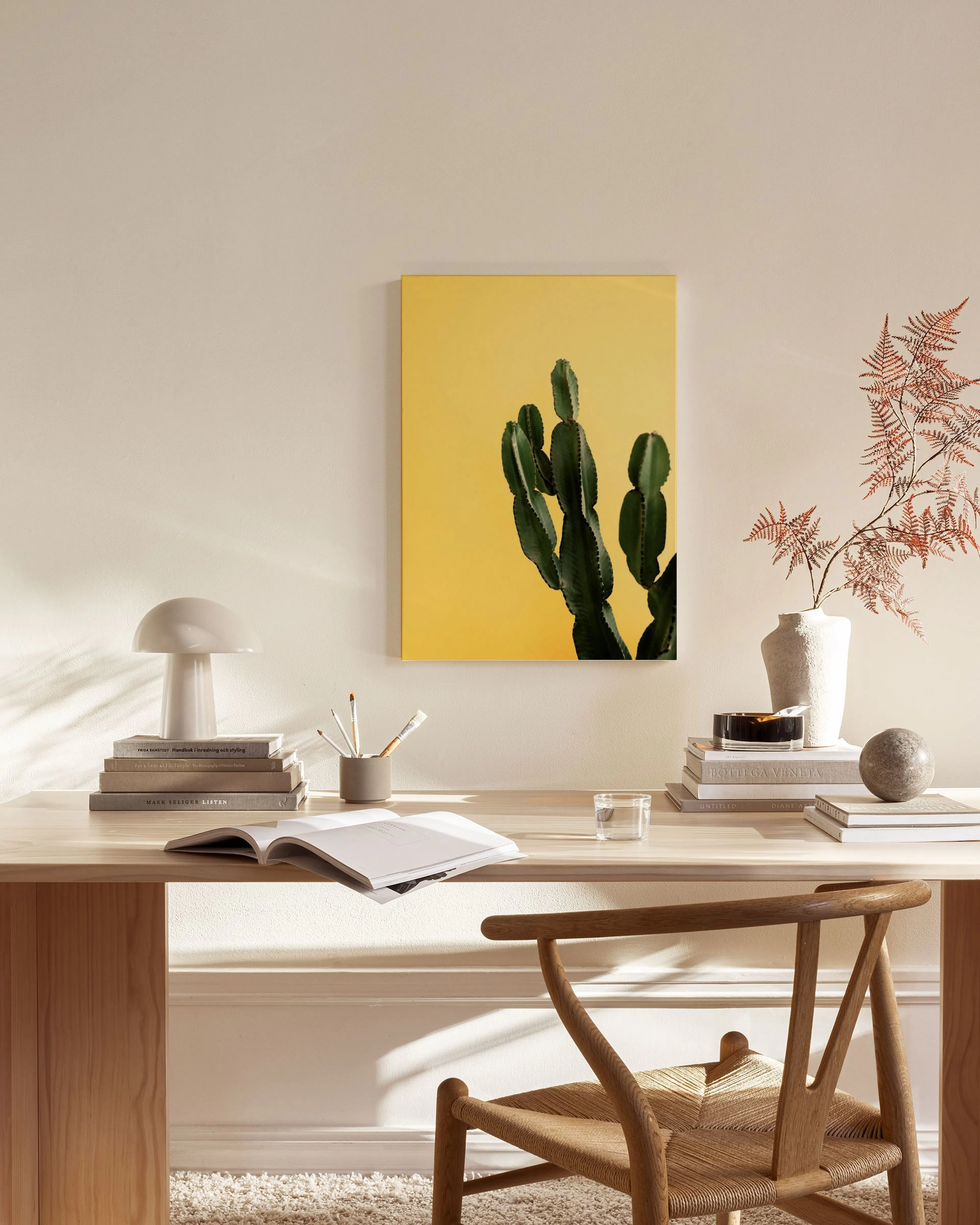 A cactus print with deep green stems against a bright yellow background, displayed in a minimal living room.