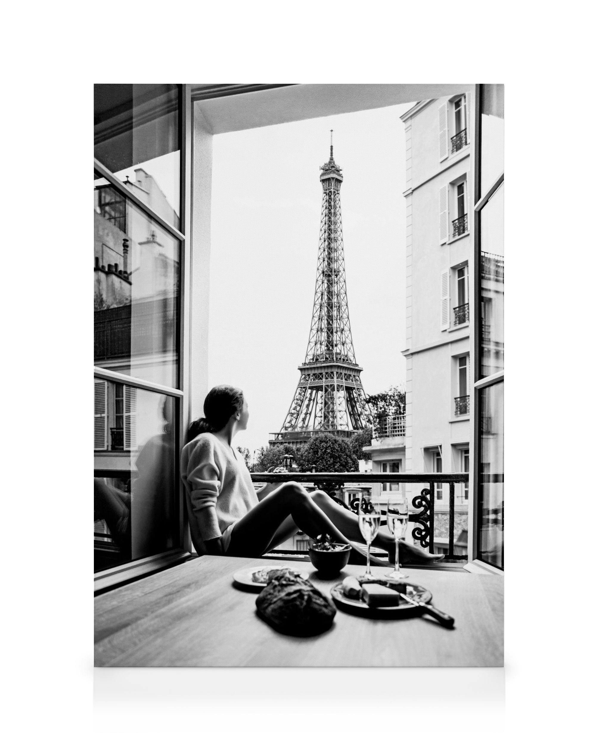 Zwart-wit canvas van een vrouw die vanuit een raam uitkijkt op de Eiffeltoren, met een tafel vol ontbijt.