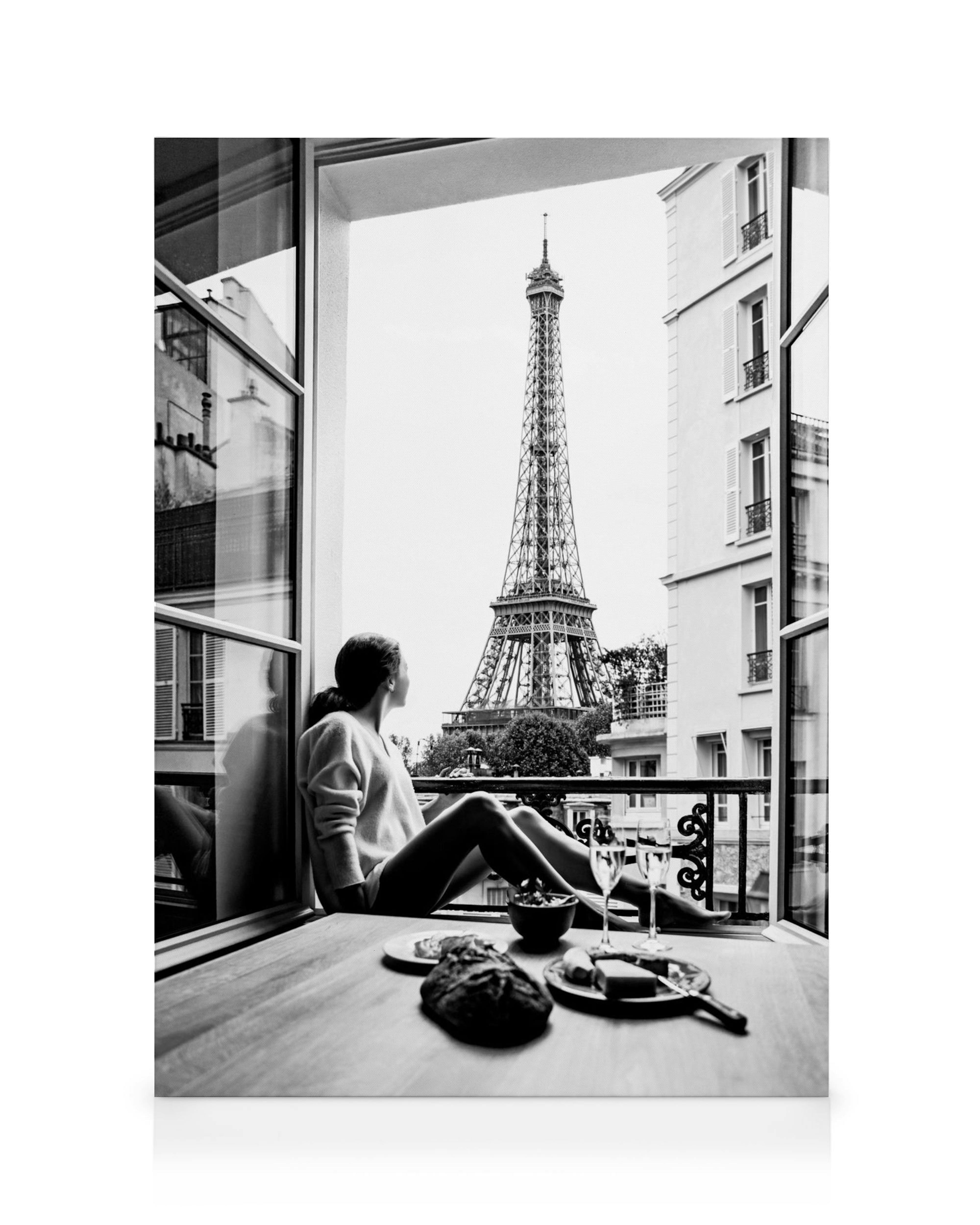 Zwart-wit canvas van een vrouw die vanuit een raam uitkijkt op de Eiffeltoren, met een tafel vol ontbijt.