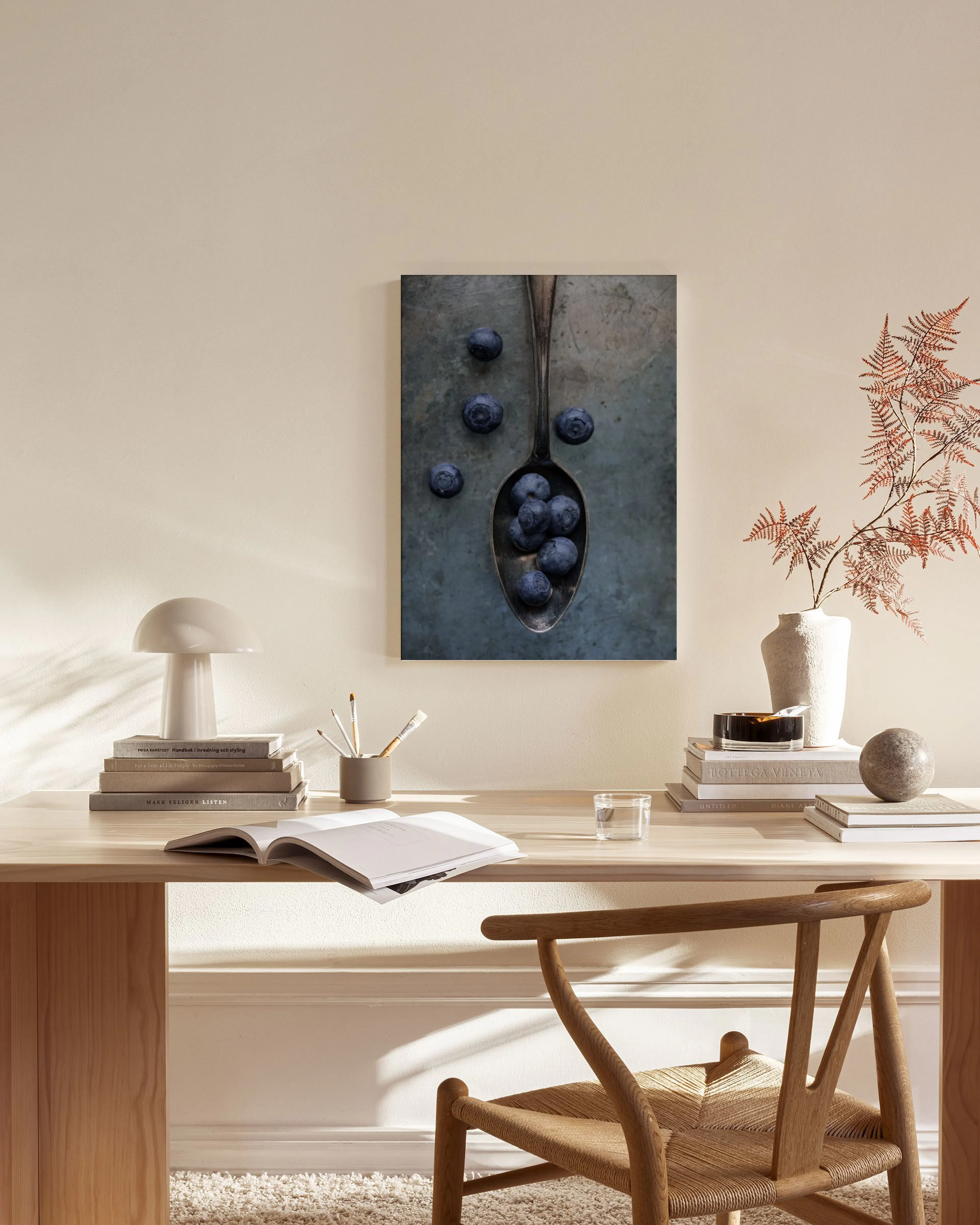 A canvas print of blueberries on a spoon, displayed above a wooden console table in a minimalist living room.