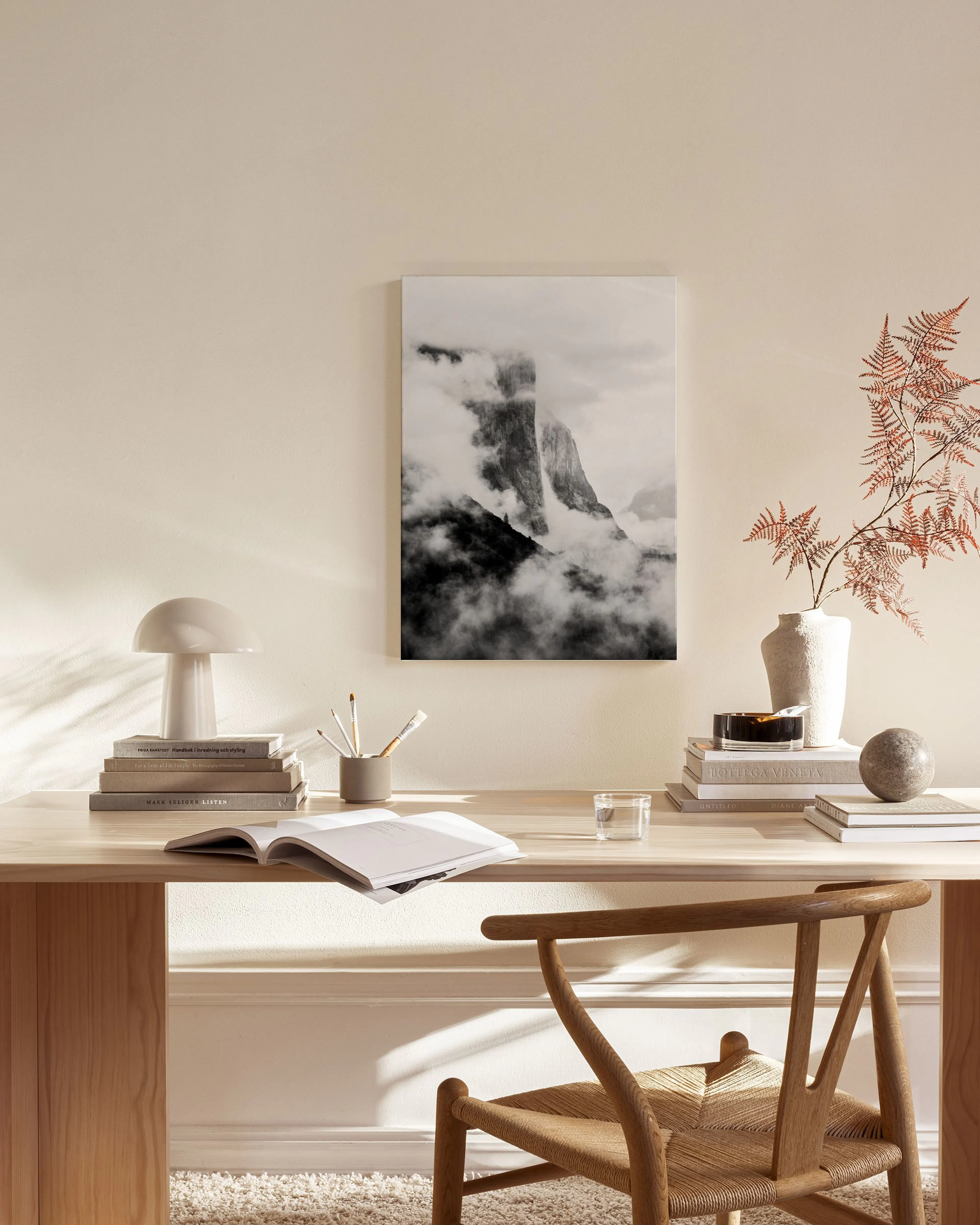 Zwart-wit canvas van een bergtop gehuld in mist, hangend in een neutrale woonkamer boven een houten dressoir.