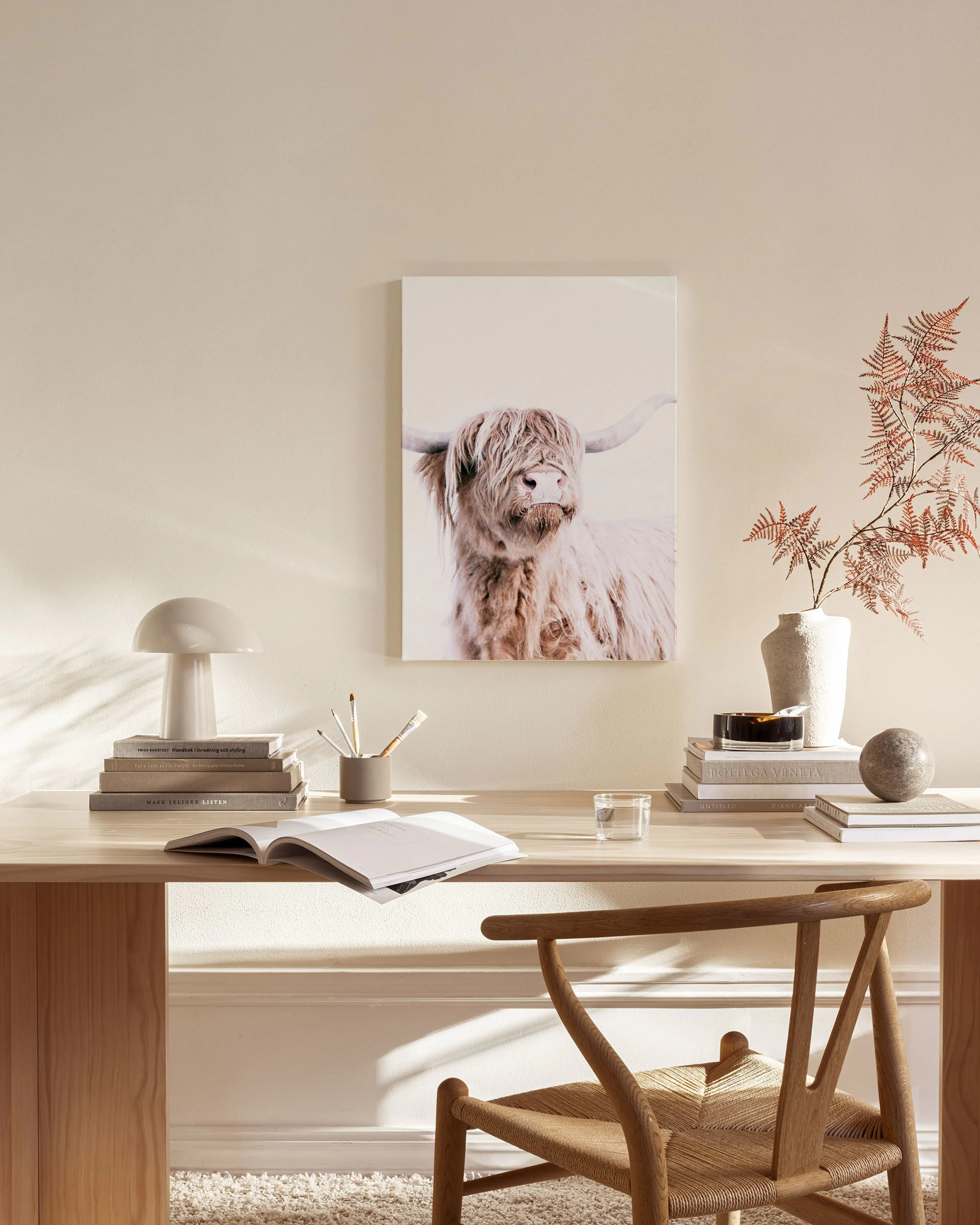 A canvas print of a shaggy Highland cow on a white background, hanging above a wooden console table in a minimalist living room.