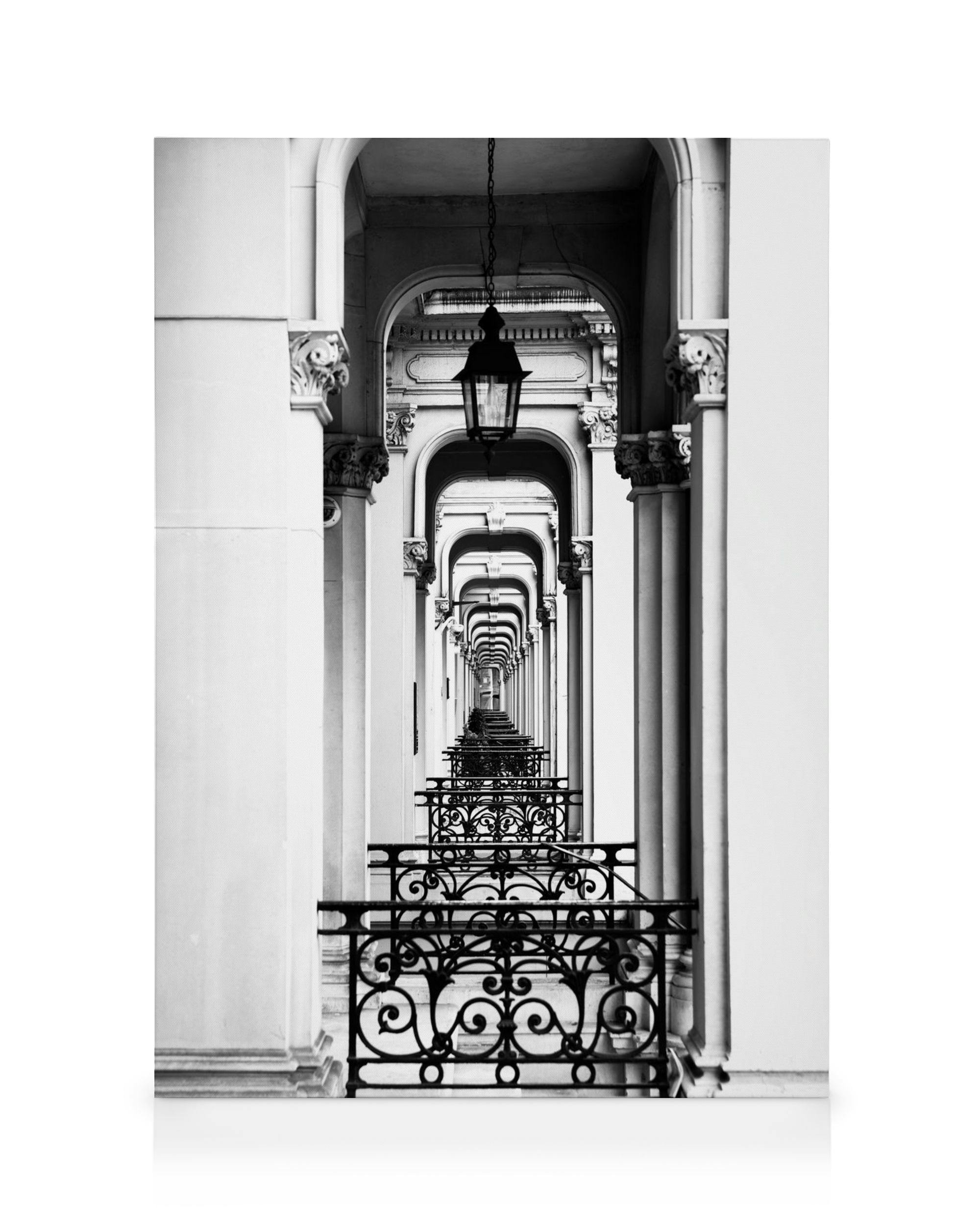 Black and white photo of a long corridor with arches and ornate railings receding into the distance, London Arch architectural a