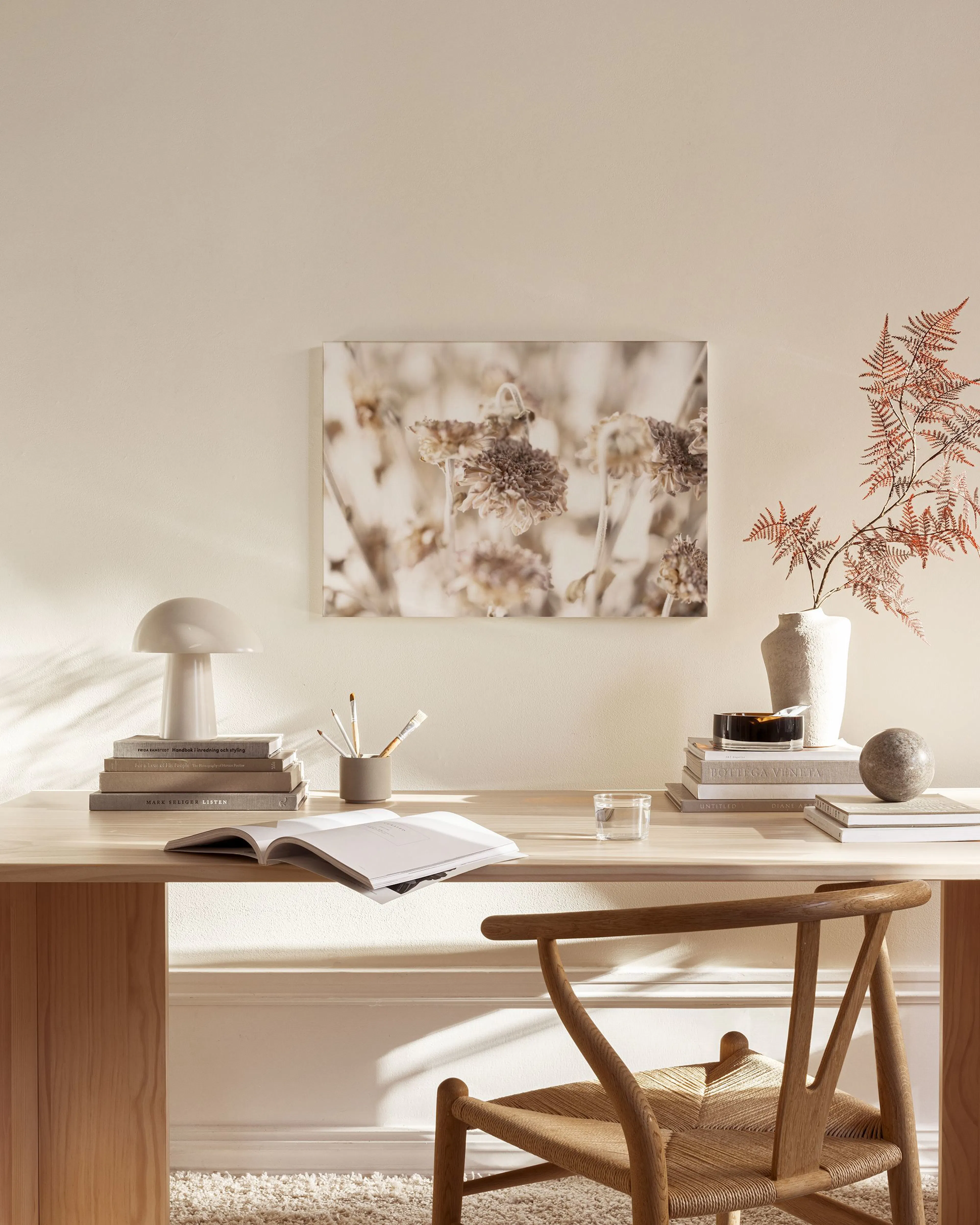 A canvas print of dried beige and brown flowers, hanging above a wooden console table in a minimalist living room.