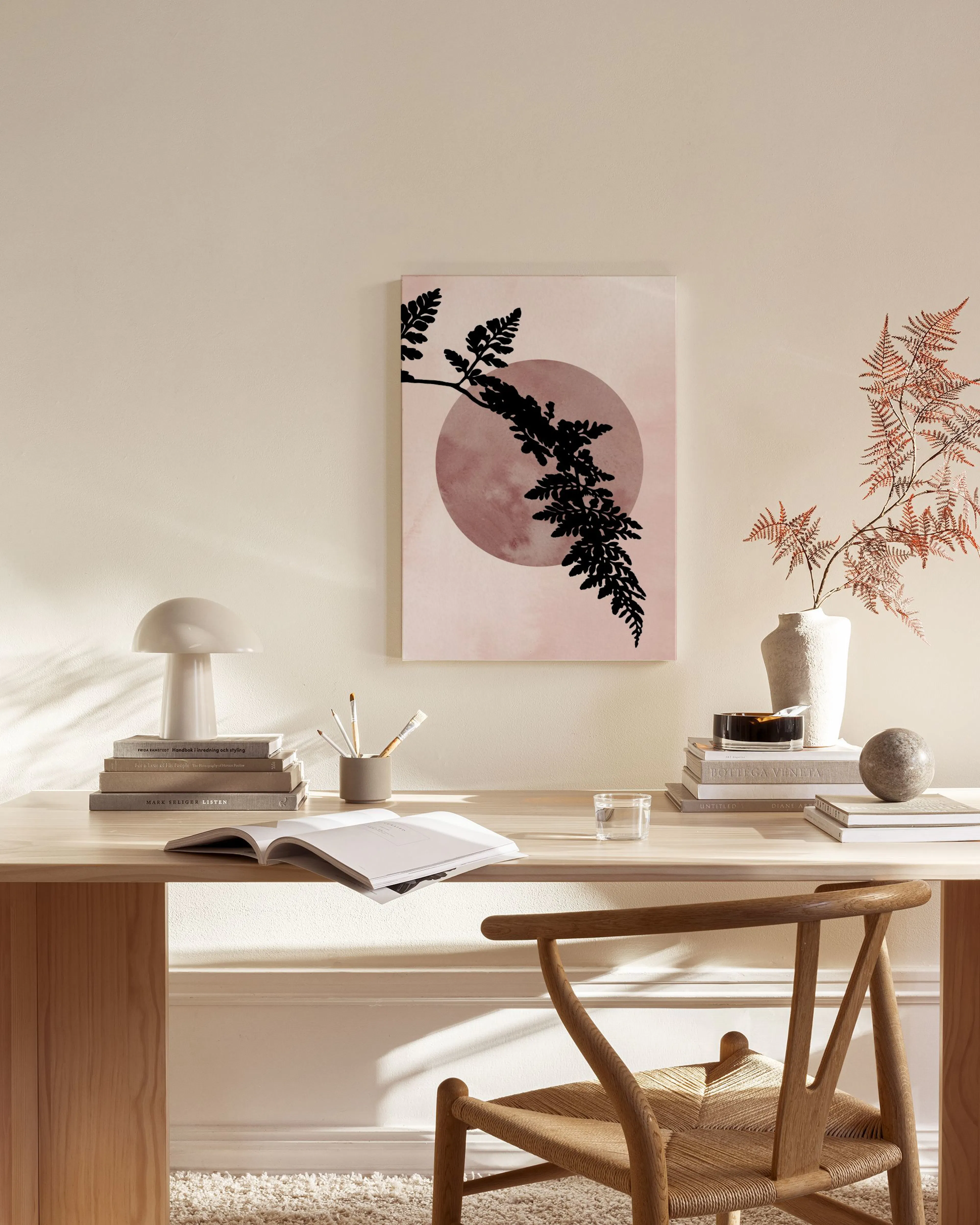 Lienzo botánico con silueta de helecho negro sobre un círculo rosa abstracto, colgado en una sala de estar.
