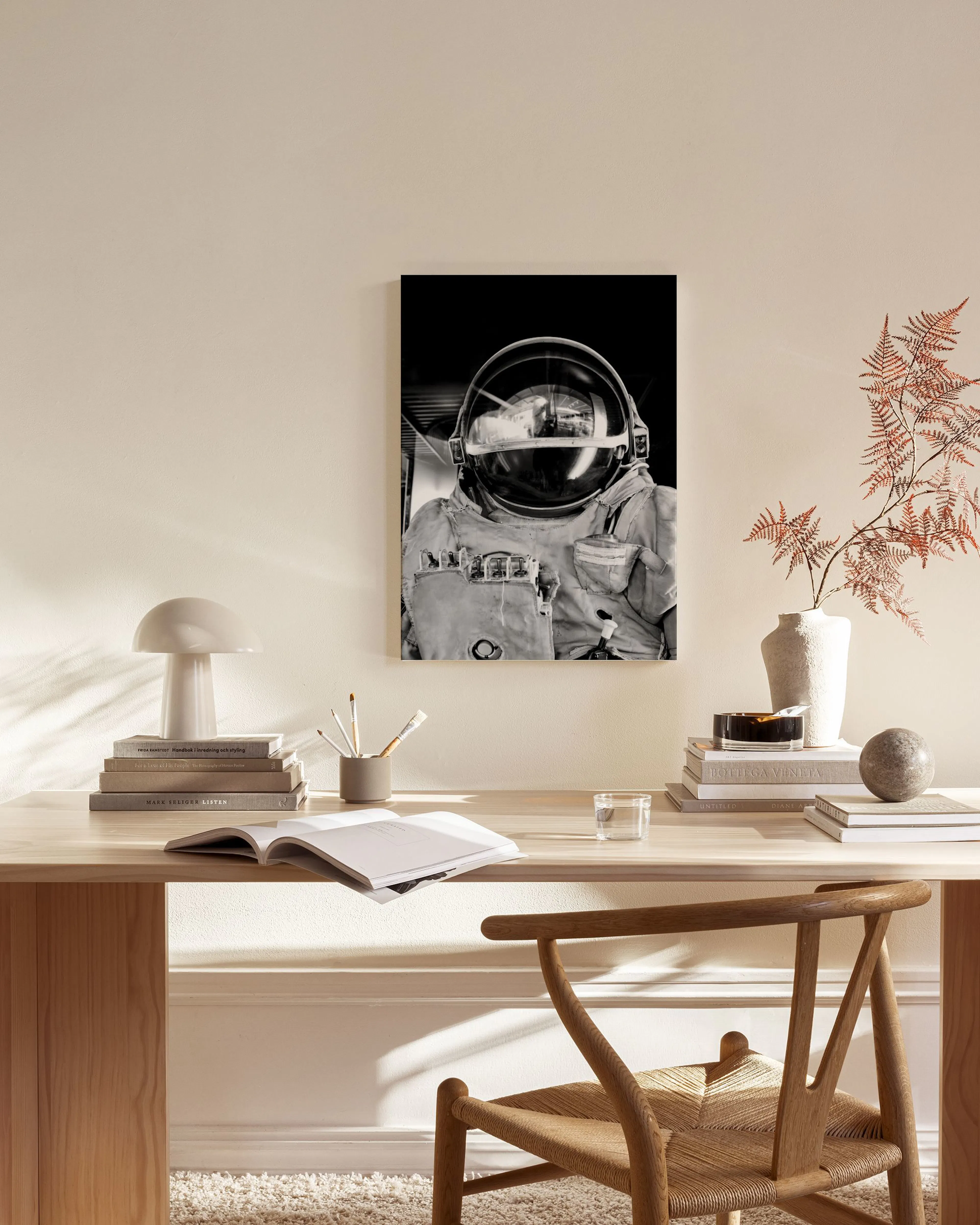 A black and white canvas print of an astronaut in a space helmet, hanging above a wooden console table in a minimalist living ro