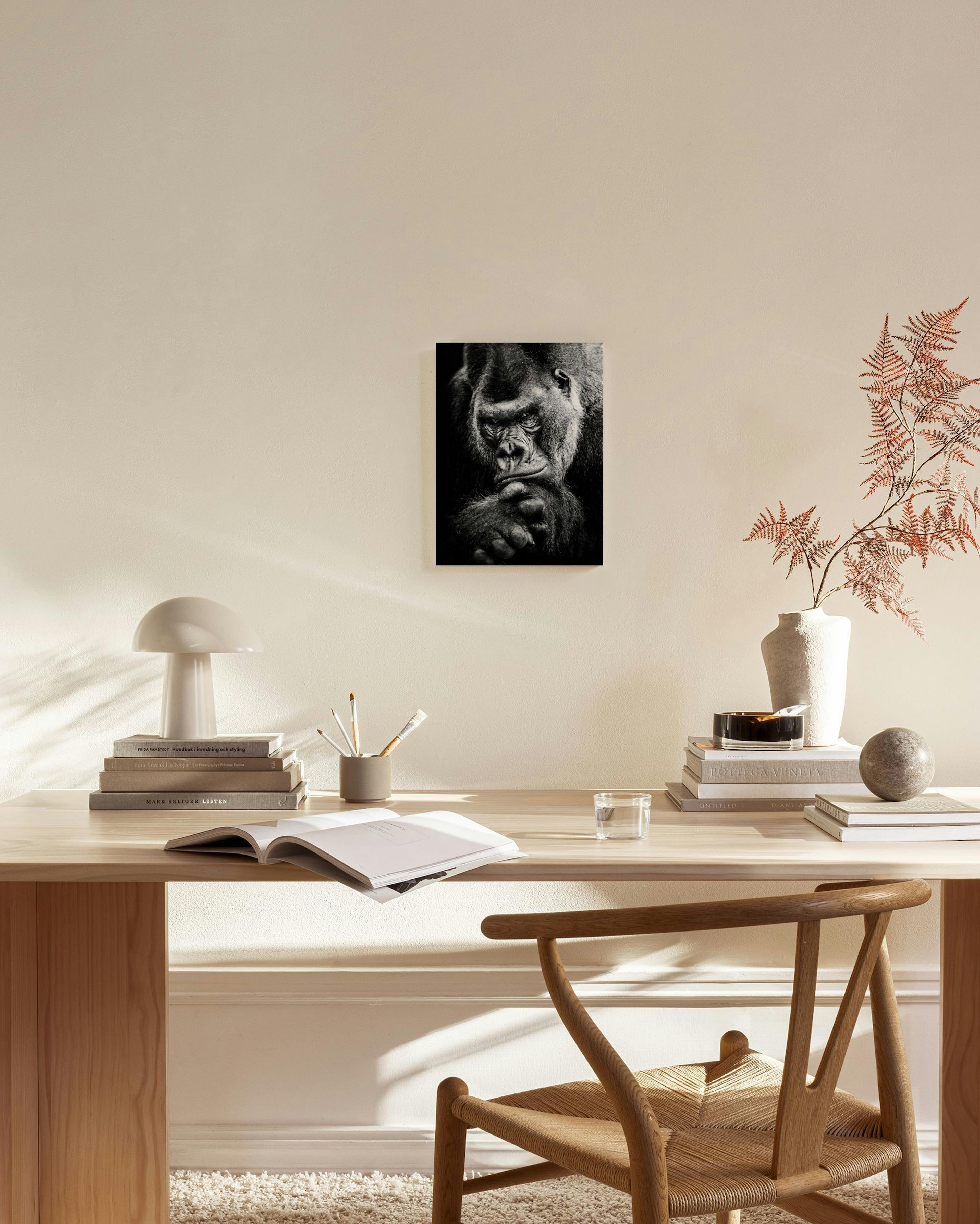 A black and white canvas print of a thoughtful gorilla, hanging in a minimalist living room above a wooden console.