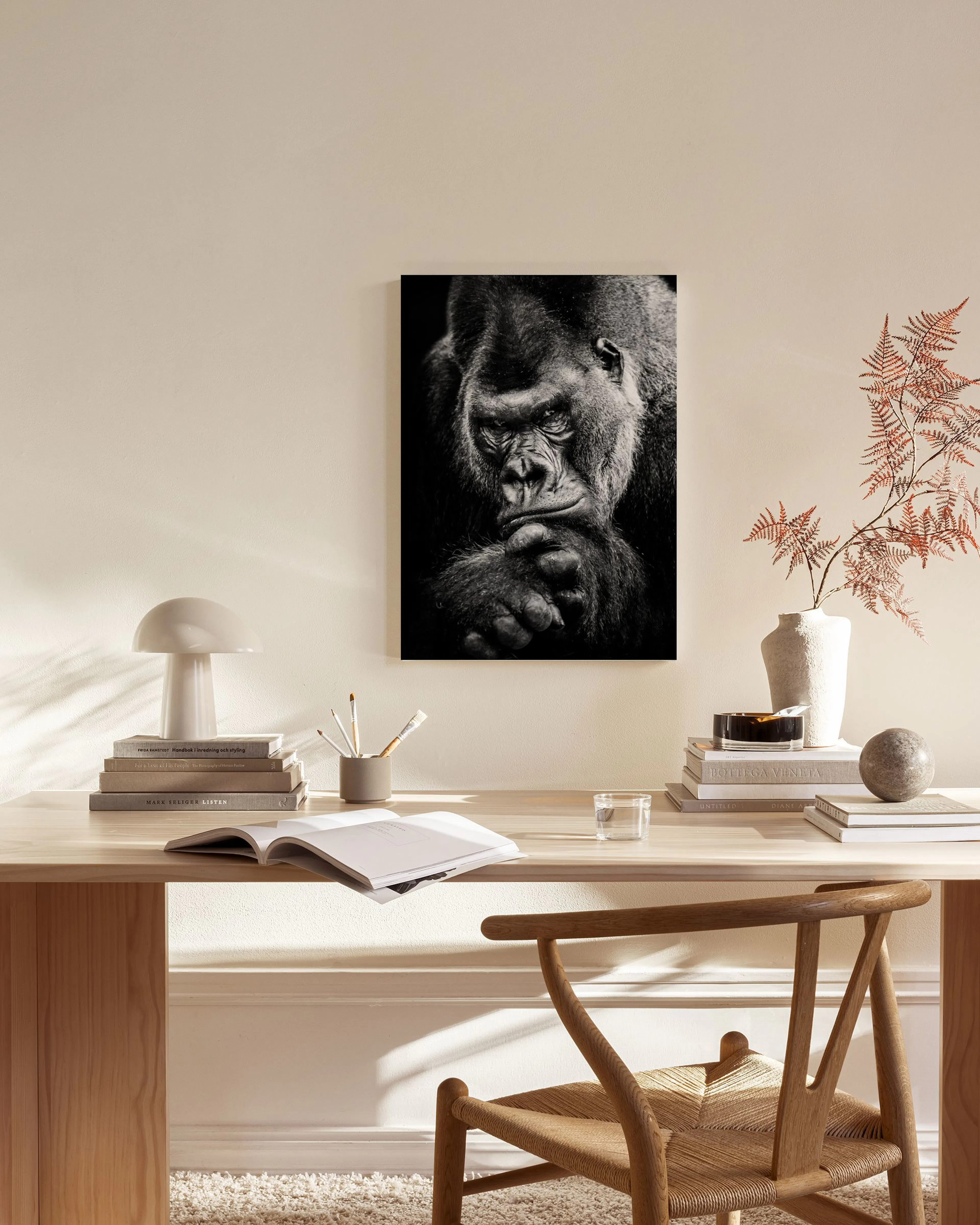 Lienzo de un gorila en blanco y negro pensativo, colgado sobre un mueble de madera en una sala moderna.
