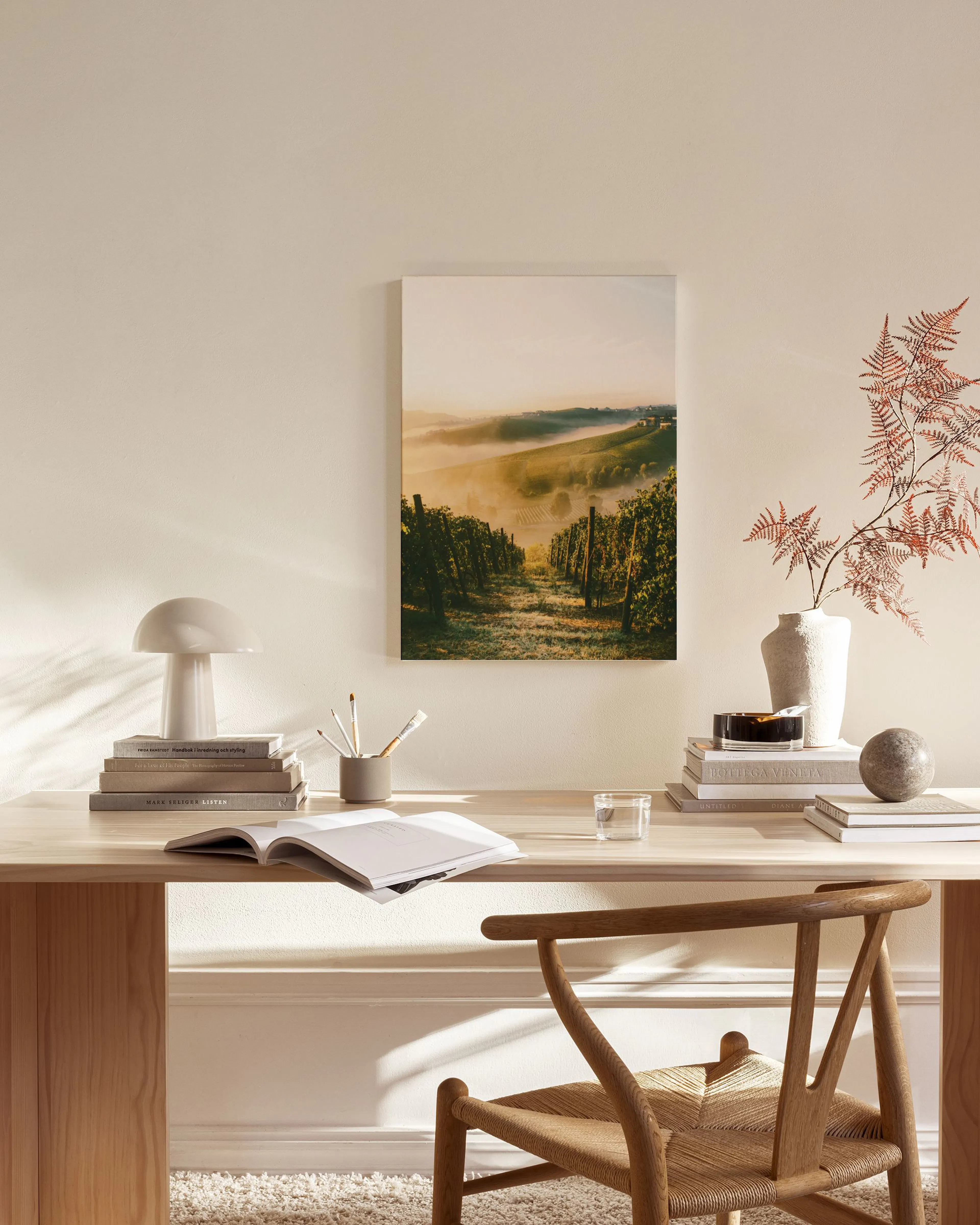 A canvas print of a morning vineyard with fog, hanging above a wooden console table in a neutral-toned living room.