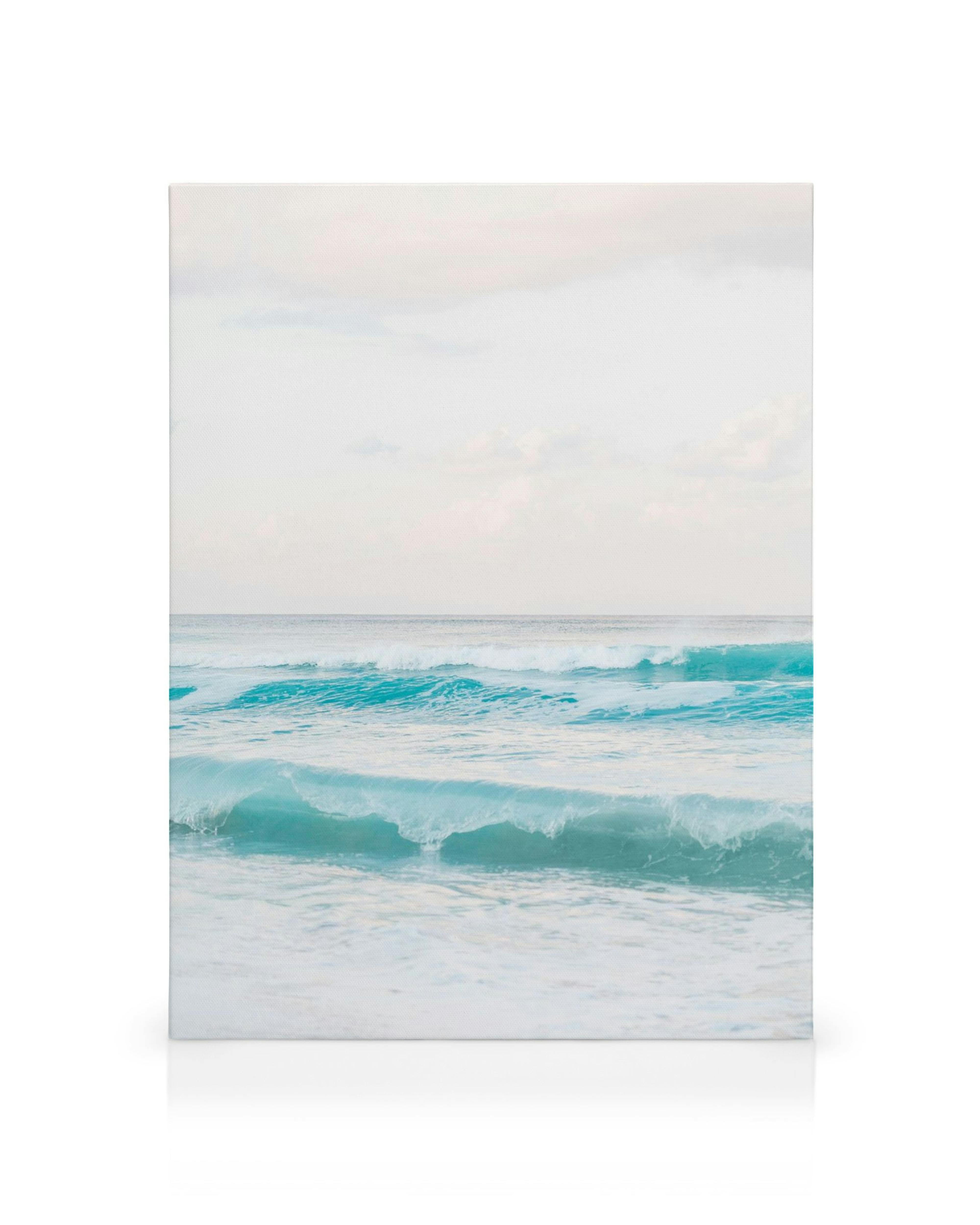 Dreamy pastel beach canvas print with soft blue waves crashing on sandy shores under a pale sky.