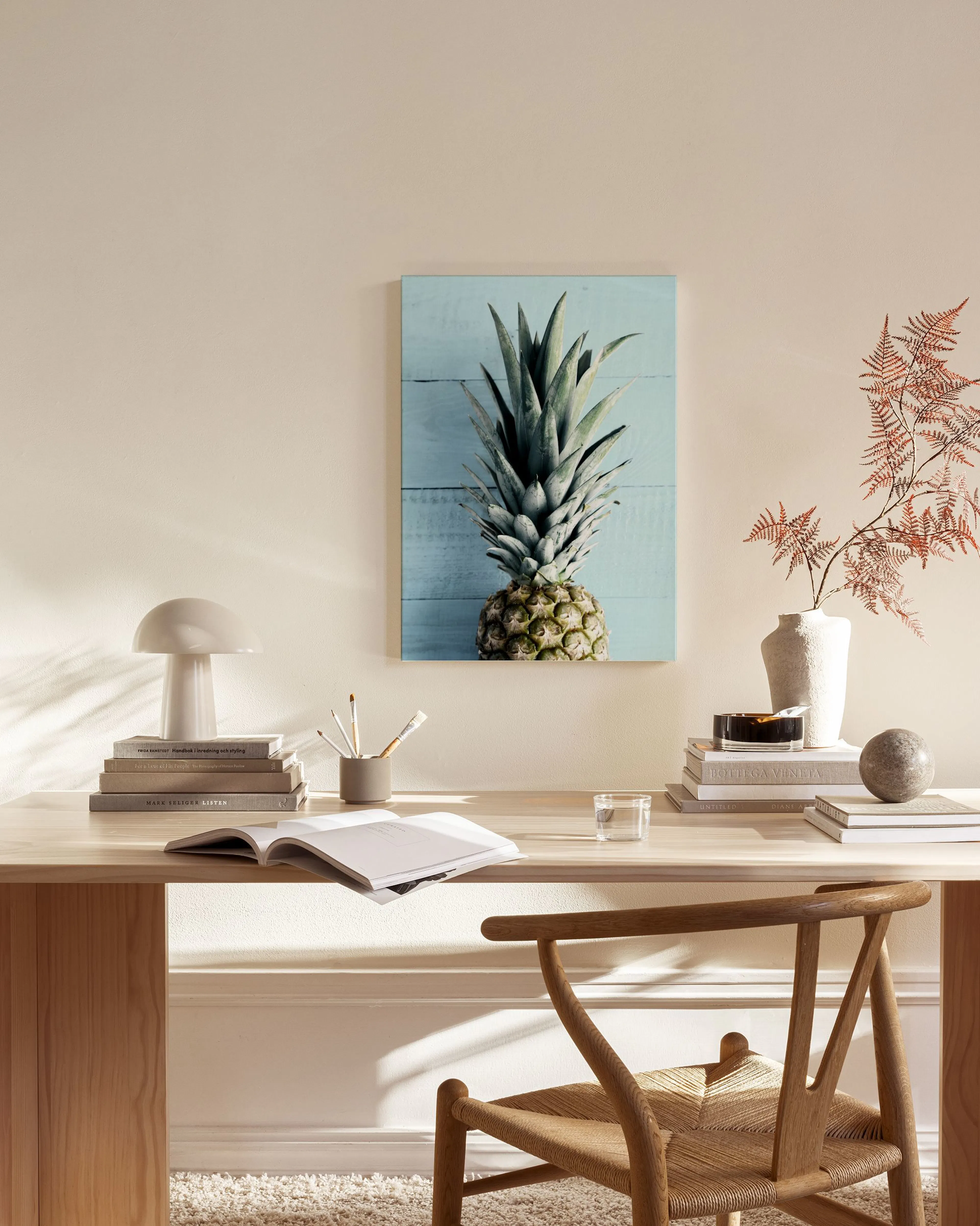 Leinwandbild einer Ananas vor hellblauer Holzoptik, über einem Beistelltisch in einem modernen Wohnzimmer.