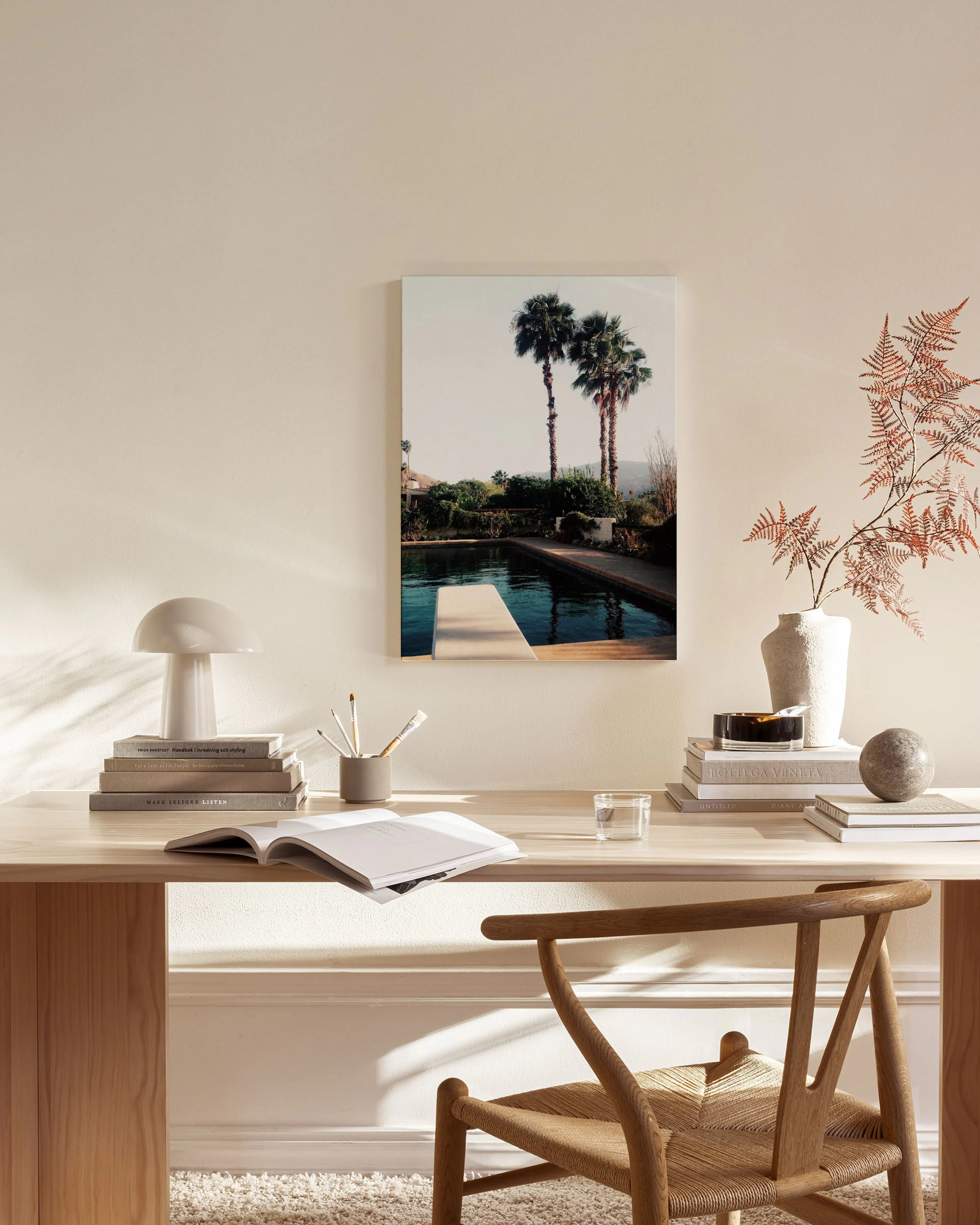 Canvas print of two palm trees by a swimming pool, displayed above a wooden console table in a minimalist living room.
