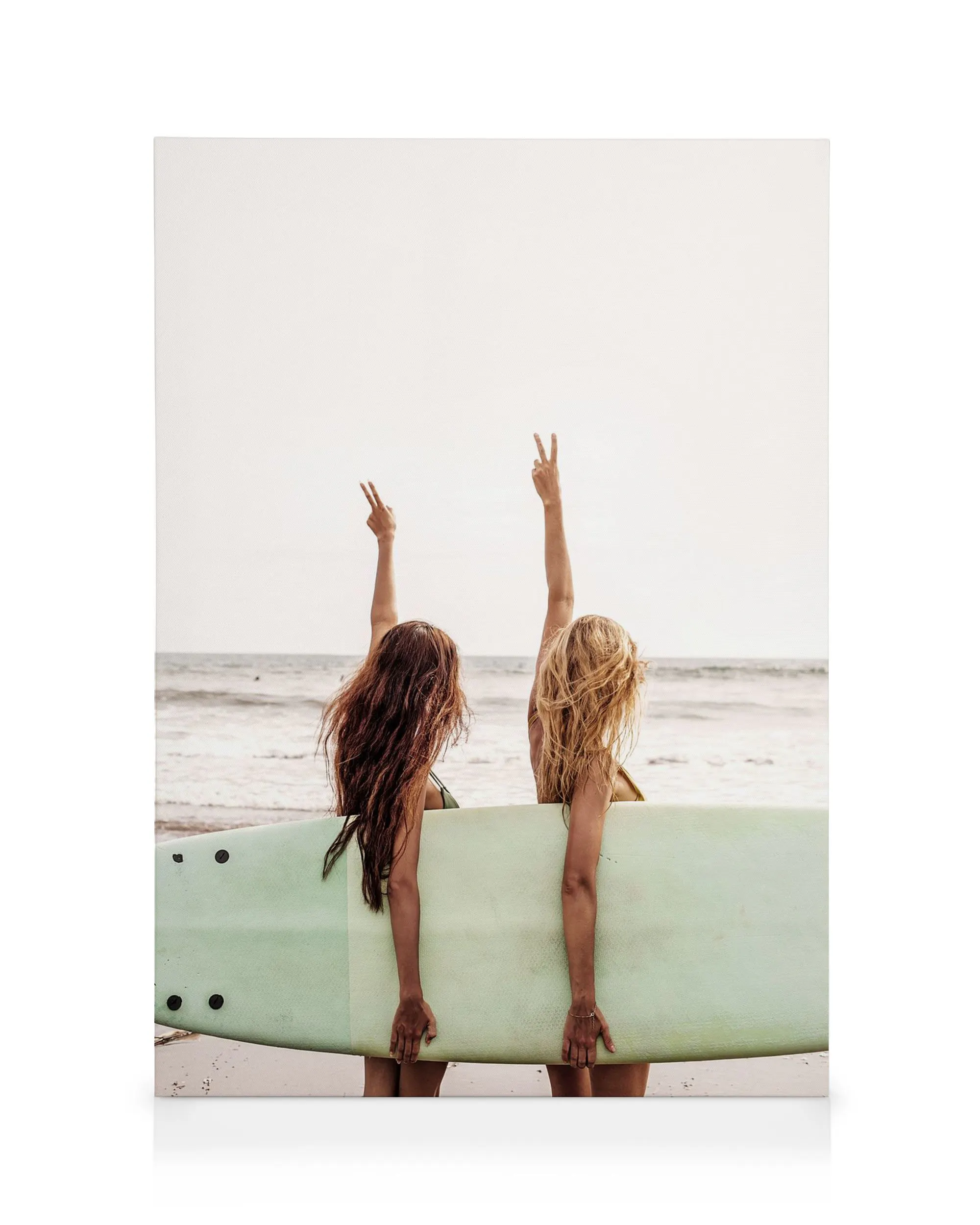 Toile de deux surfeuses aux cheveux longs, de dos, tenant une planche de surf, faisant le signe de la paix, sur une plage.