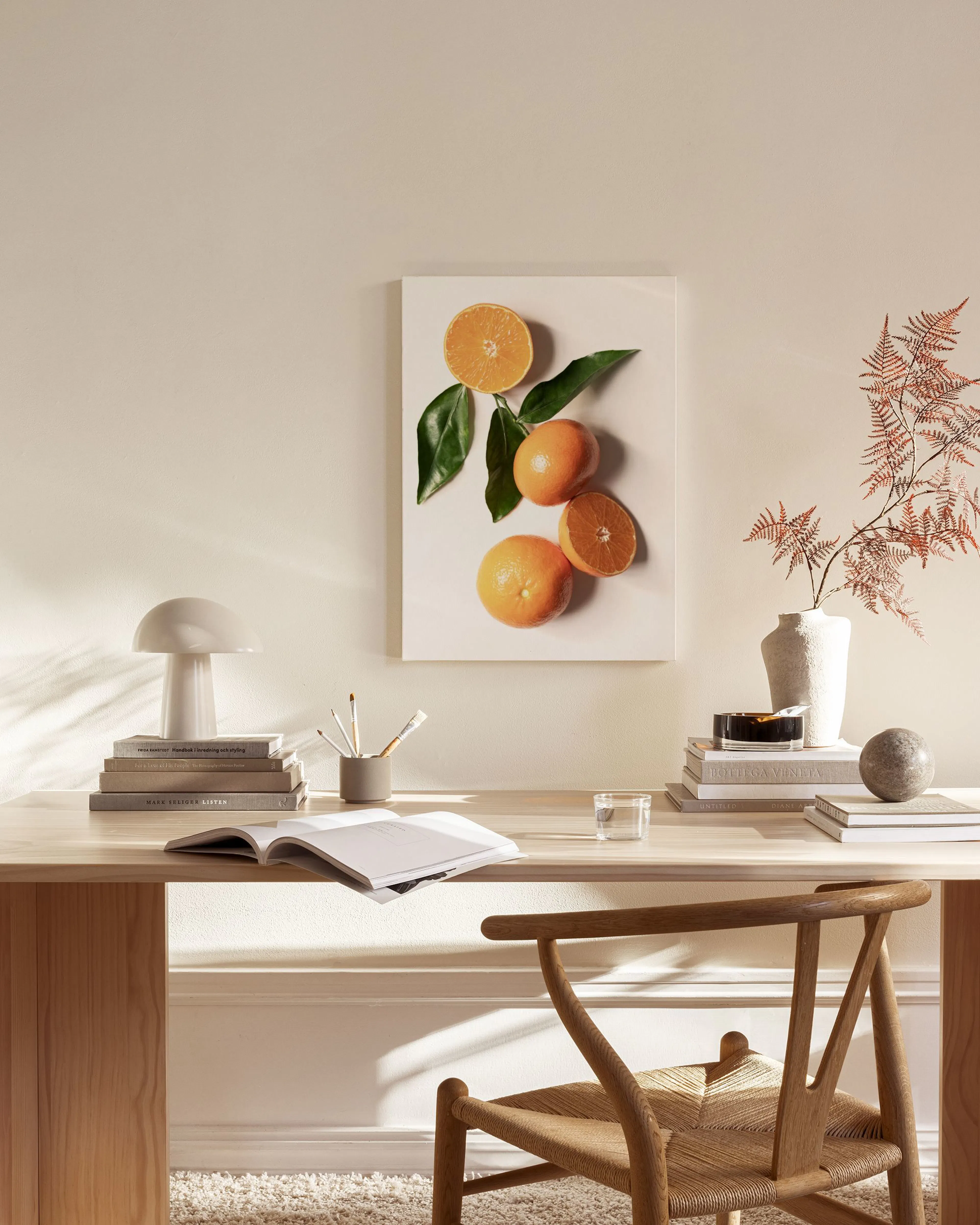 A canvas print of whole and sliced oranges with green leaves, hanging above a wooden console in a minimalist living room.