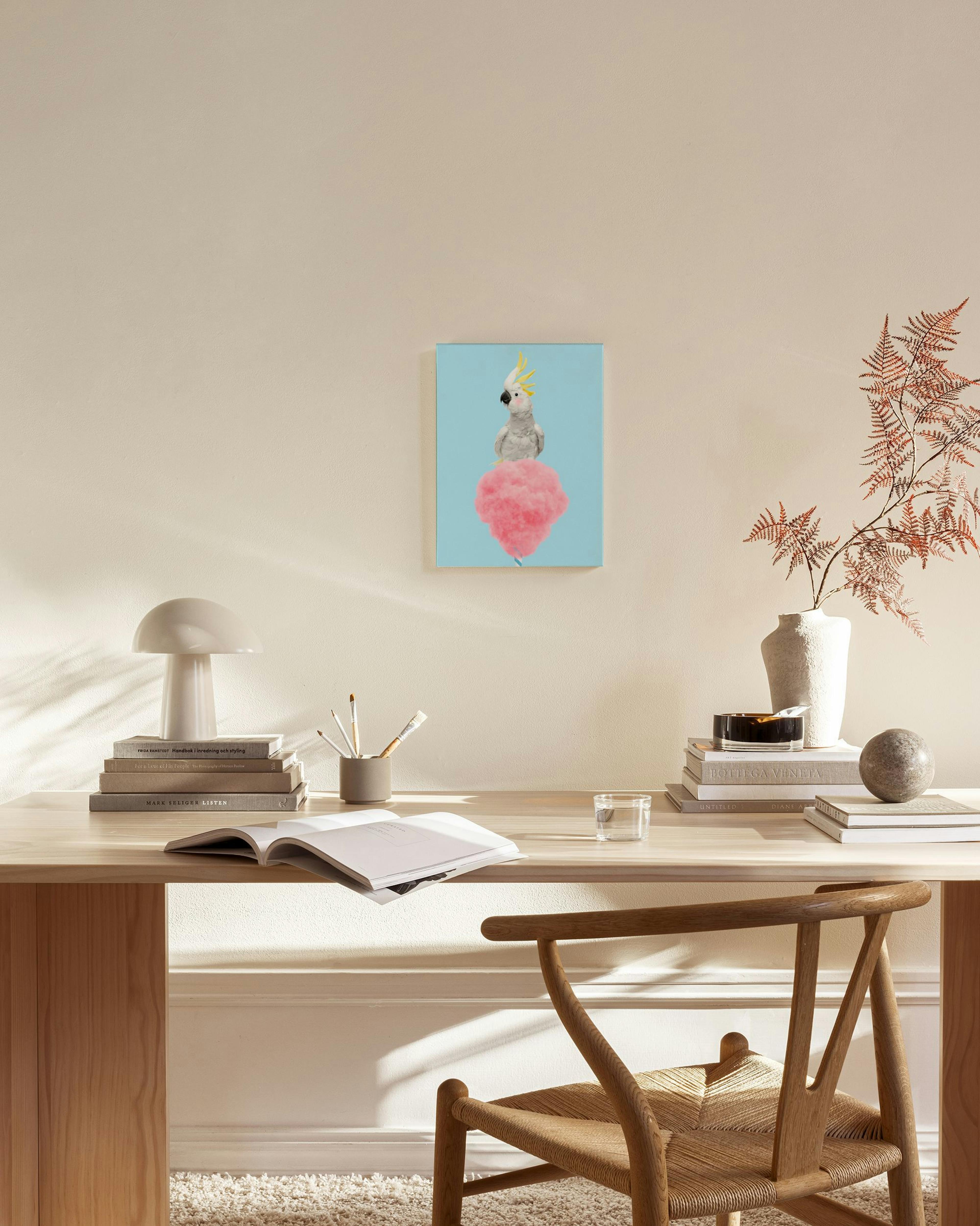 Een canvas met een kaketoe op roze suikerspin op een lichtblauwe achtergrond, hangend in een moderne woonkamer.