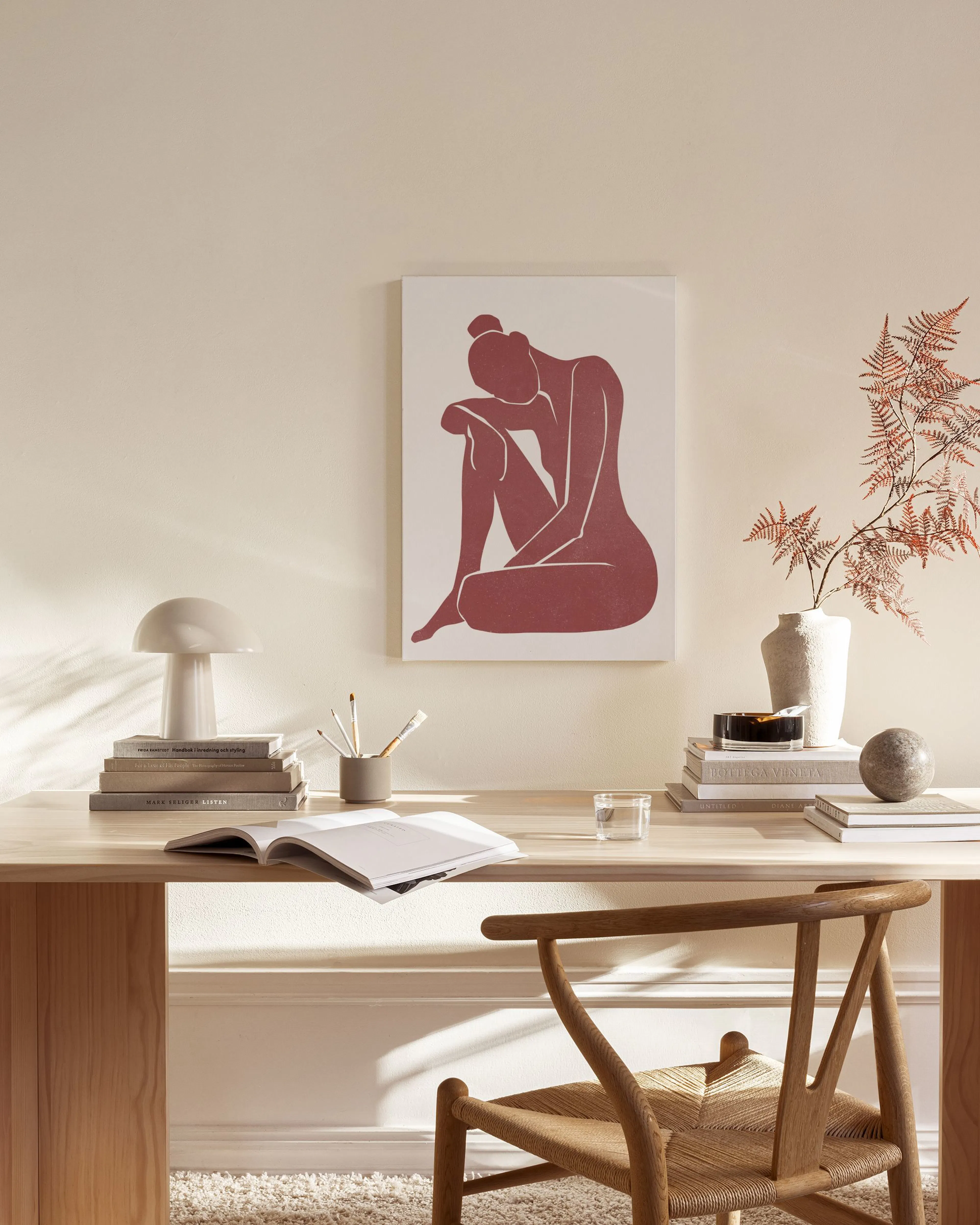 Toile dune silhouette féminine rouge foncé sur fond blanc, suspendue dans un salon moderne aux tons neutres.