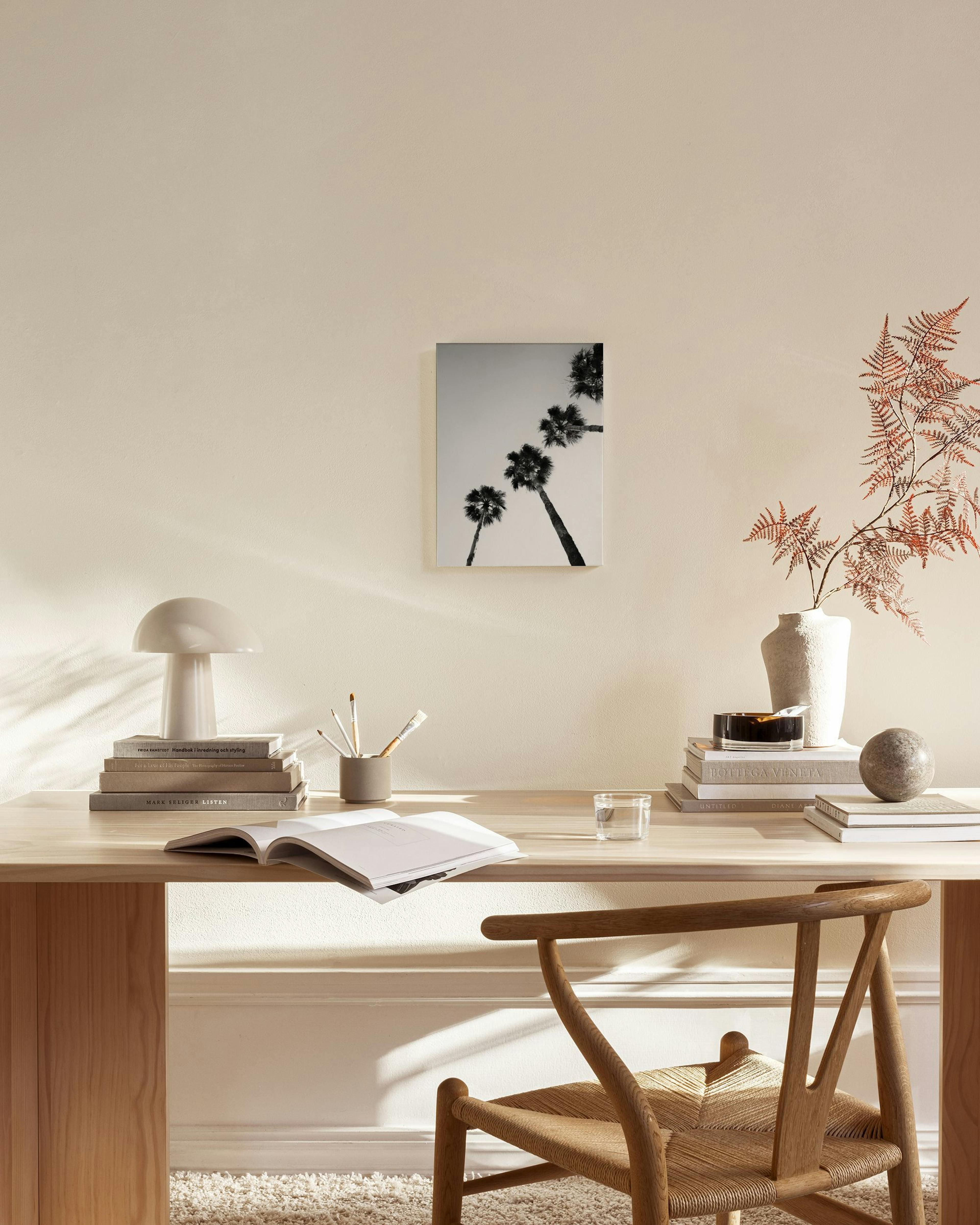 Schwarz-weißes Leinwandbild mit schräg aufsteigenden Palmen, hängend über einem Sideboard in einem hellen Wohnzimmer.