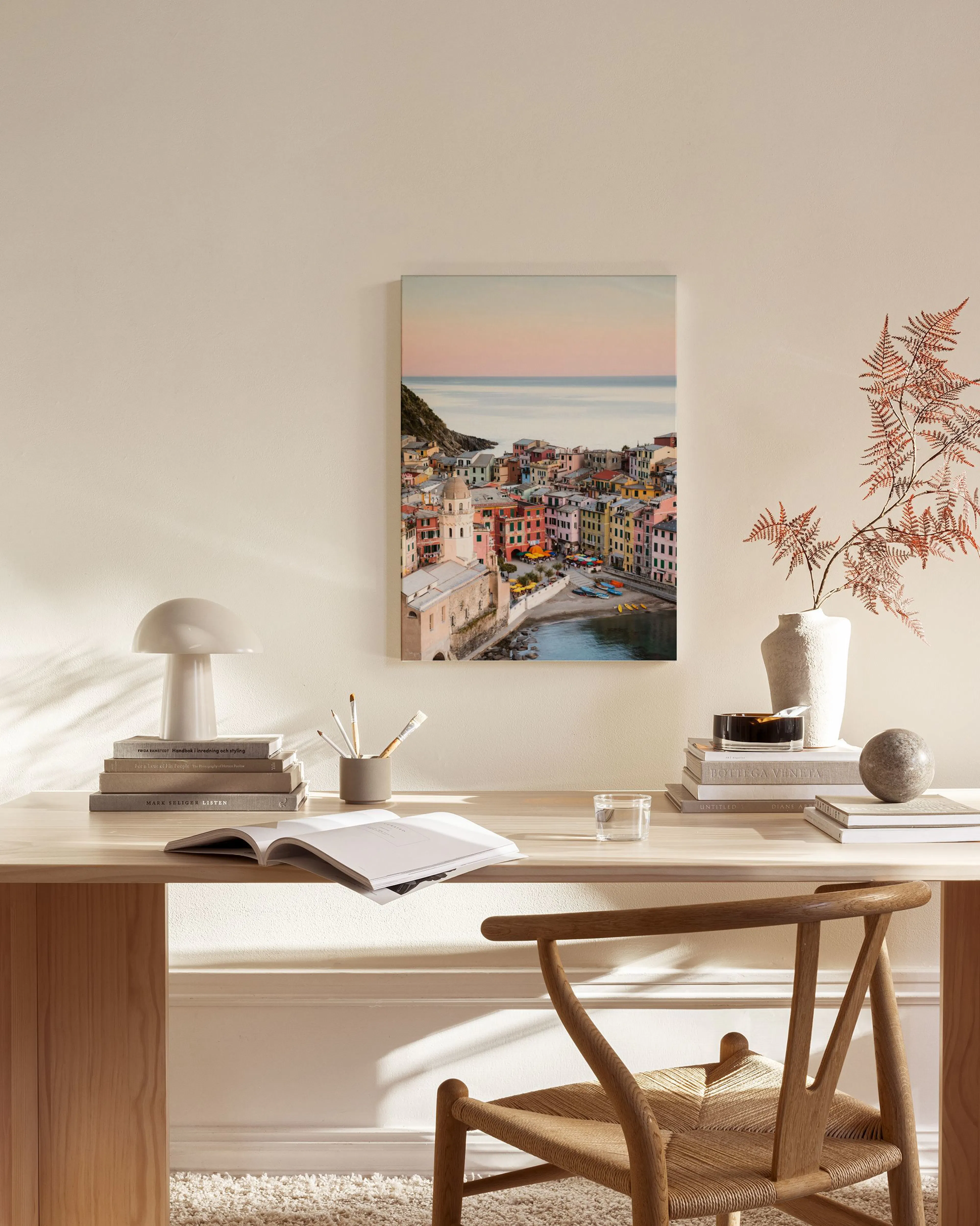 Stampa su tela di un borgo colorato sul mare al tramonto, appesa sopra una panca in un ambiente moderno.