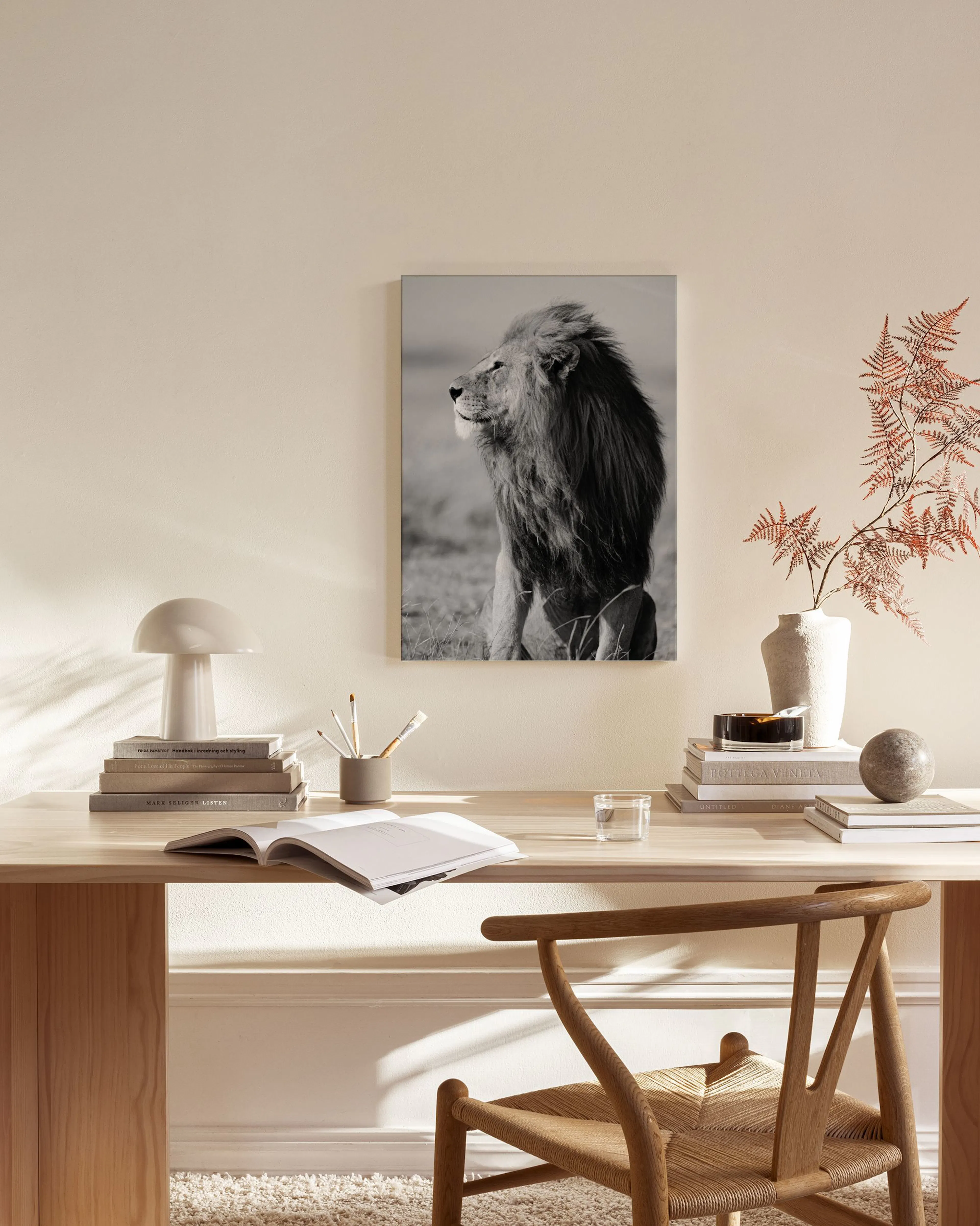 Zwart-wit canvas van een majestueuze leeuw in een serene omgeving, hangend boven een houten dressoir in een lichte woonkamer.
