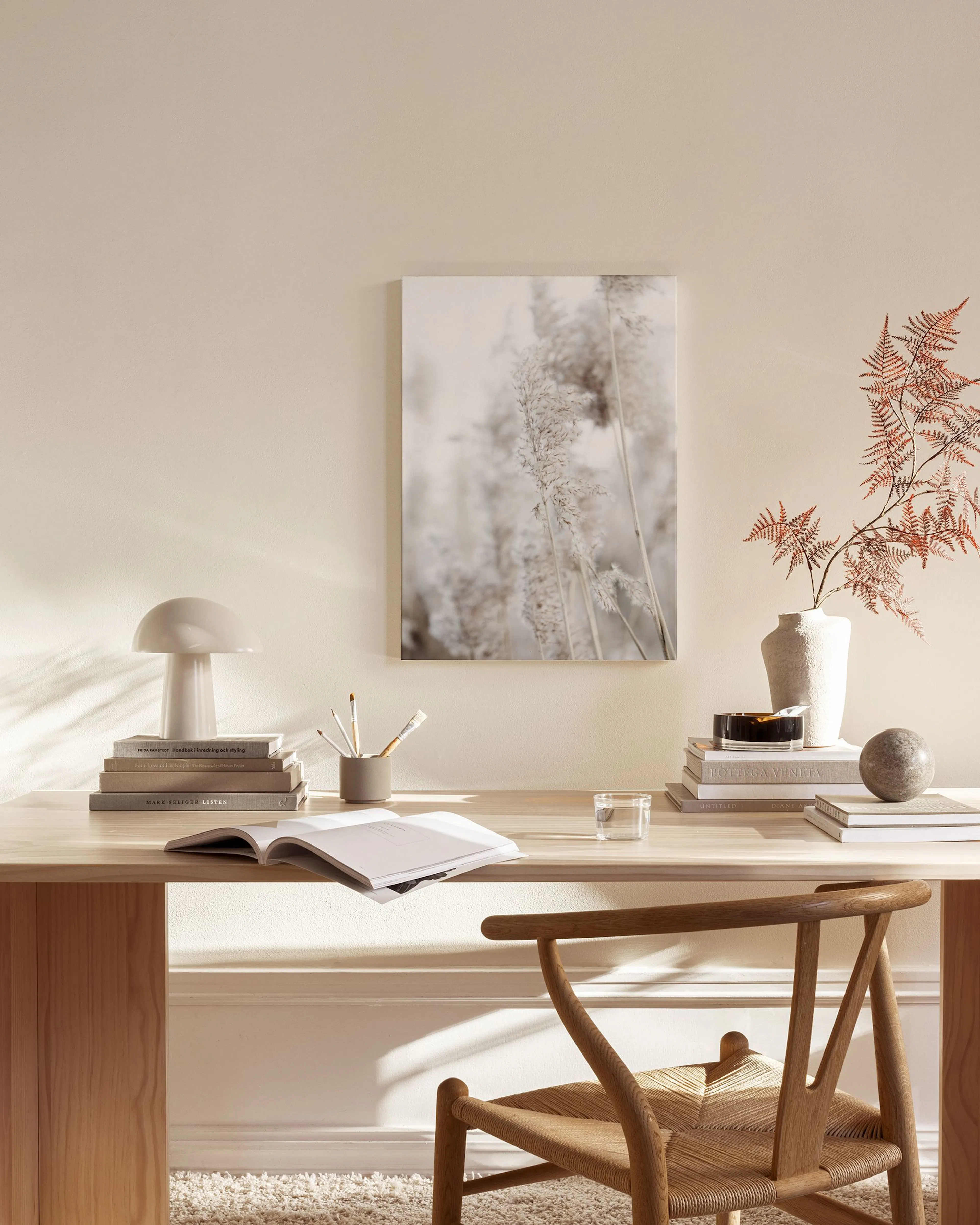 A canvas print of feathery brown and white reeds, hanging in a neutral-toned living room above a wooden console.