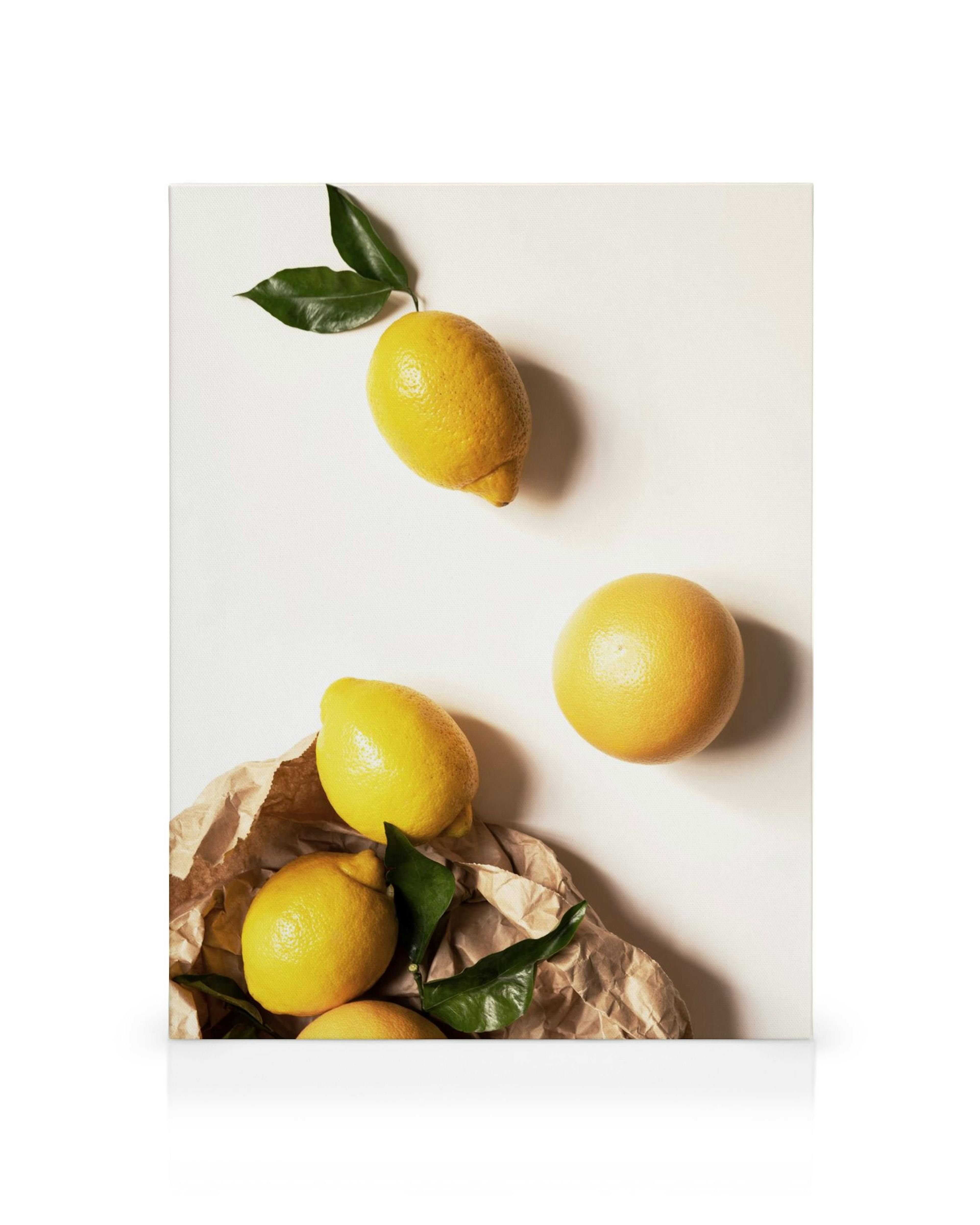 Yellow lemons with vibrant green leaves on brown paper, citrus fruit still life canvas print.