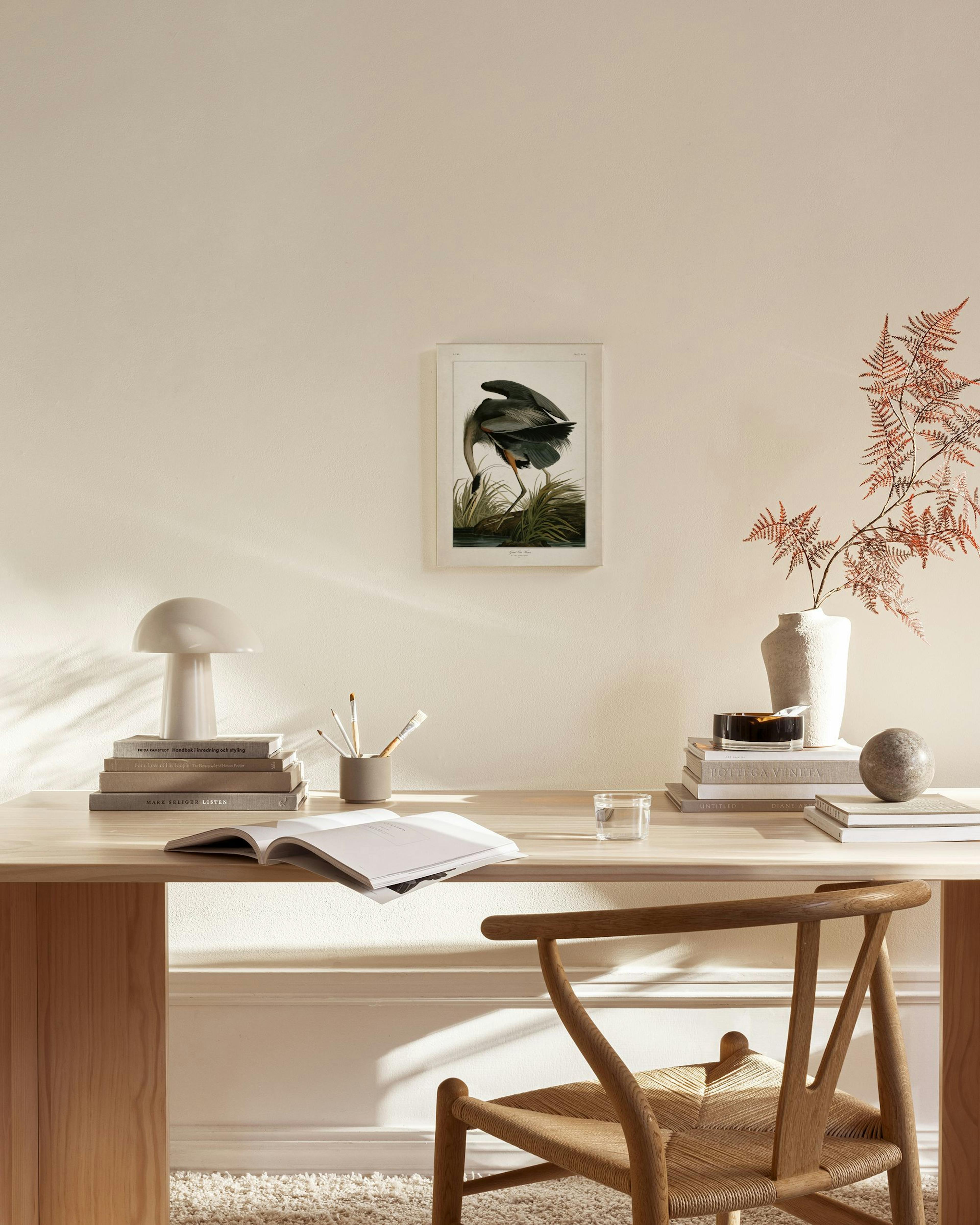 Toile dun héron bleu dans lherbe, suspendue au-dessus dun banc en bois clair dans un salon à la décoration épurée.