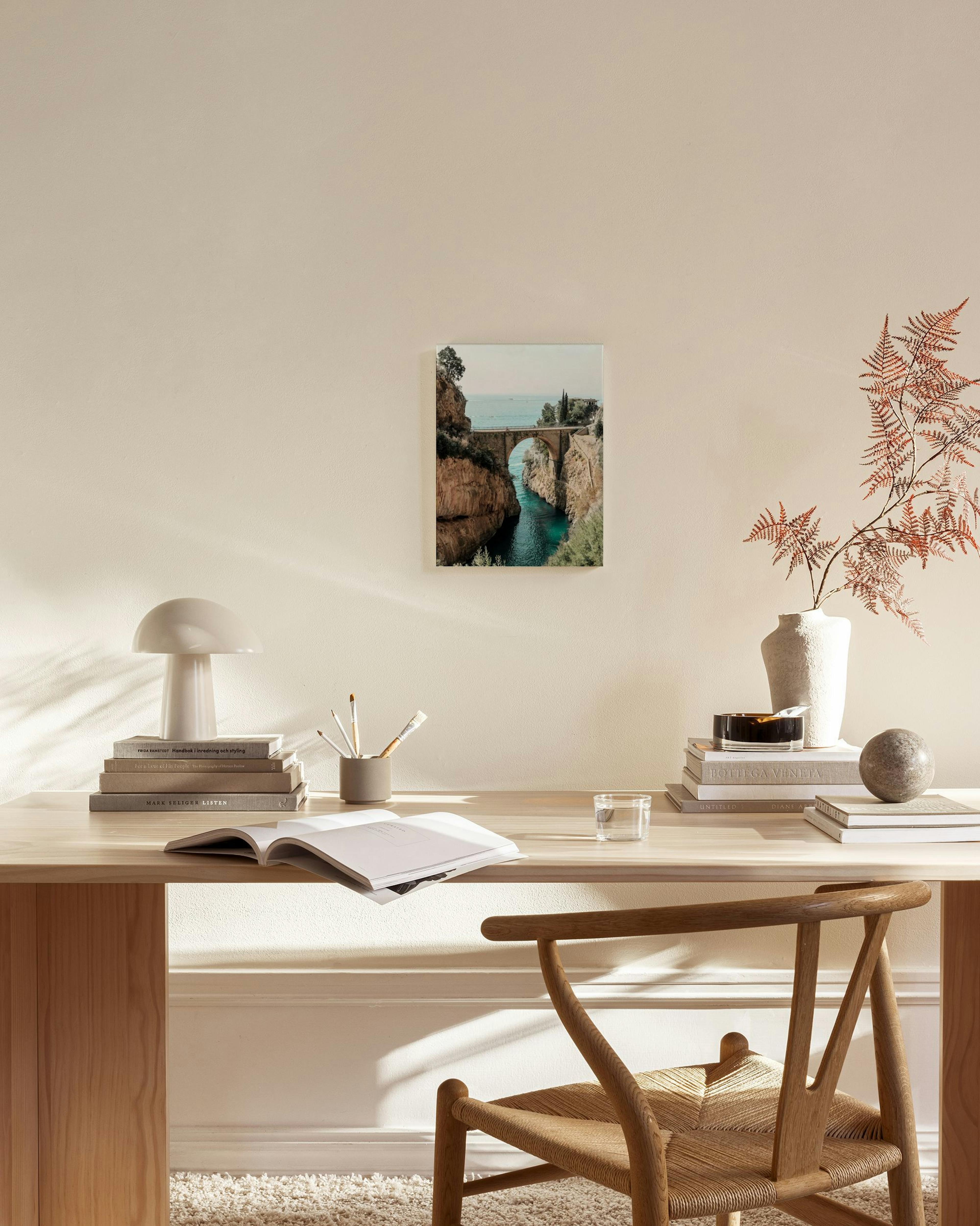 A canvas print of an arched stone bridge over a blue river in a rocky canyon, hanging in a minimalist living room.