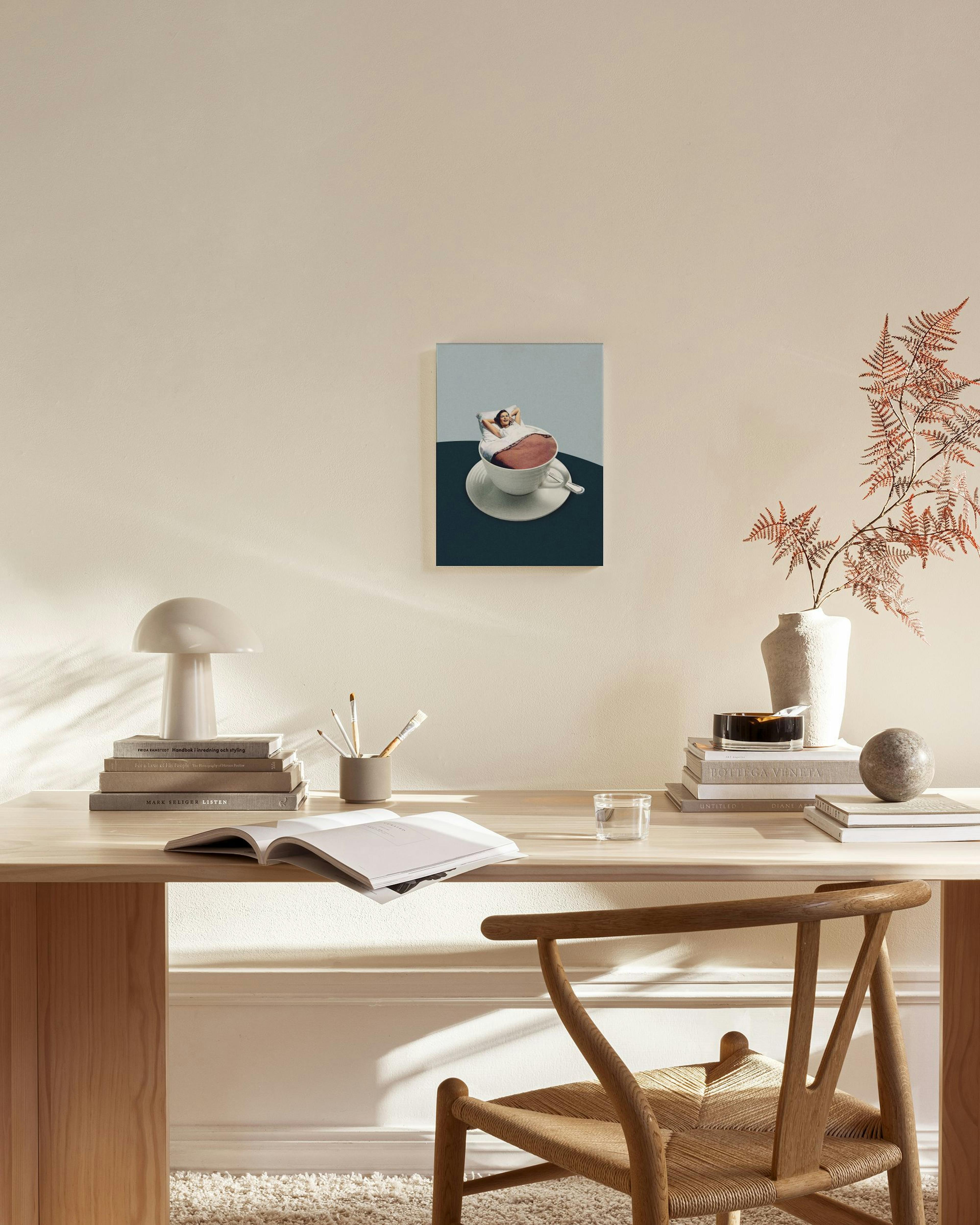 A canvas print of a person relaxing in a large teacup, hanging on a light wall in a minimalist living room.