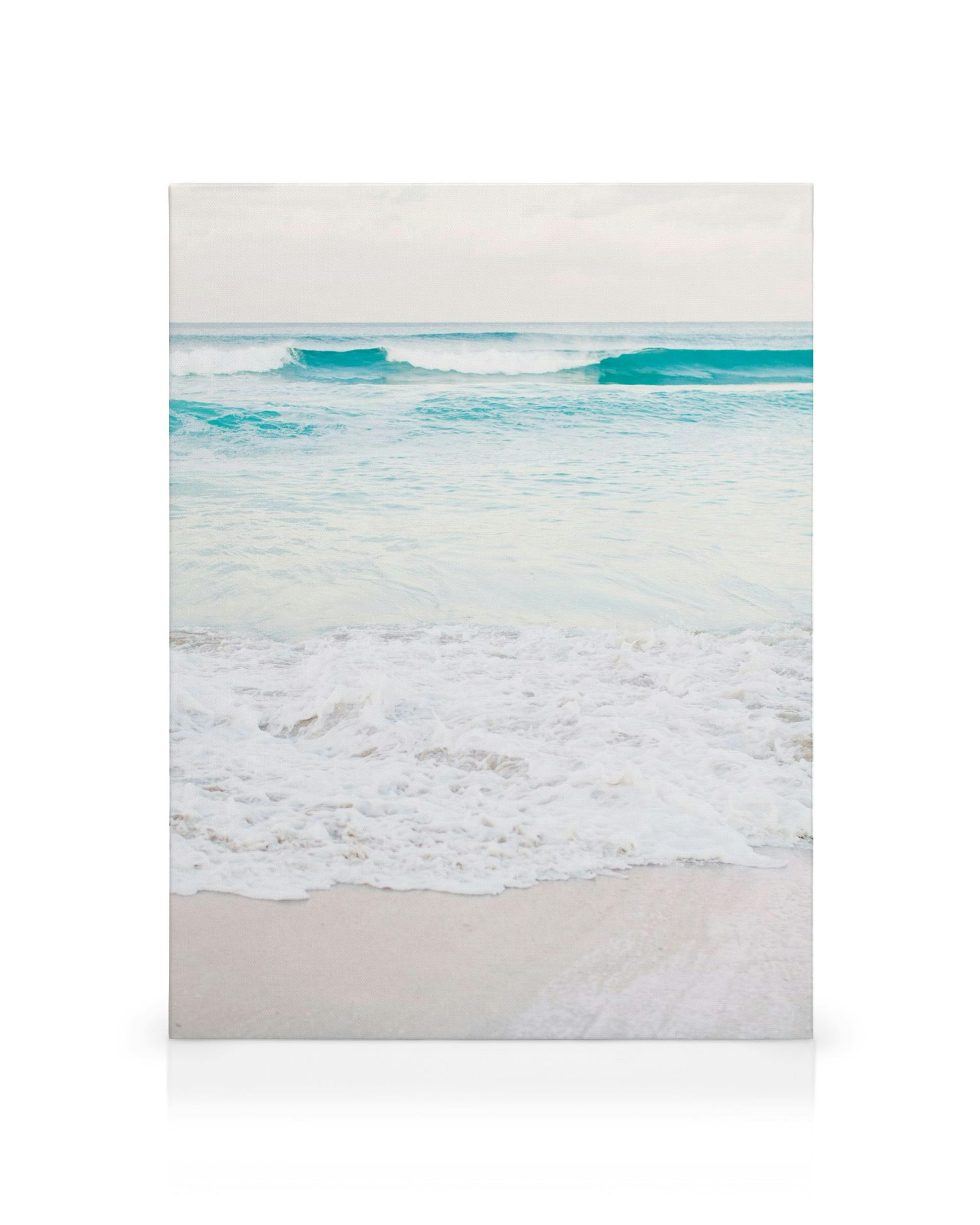 Toile de plage de sable avec des vagues océaniques bleu clair et de la mousse blanche, sous un ciel pâle