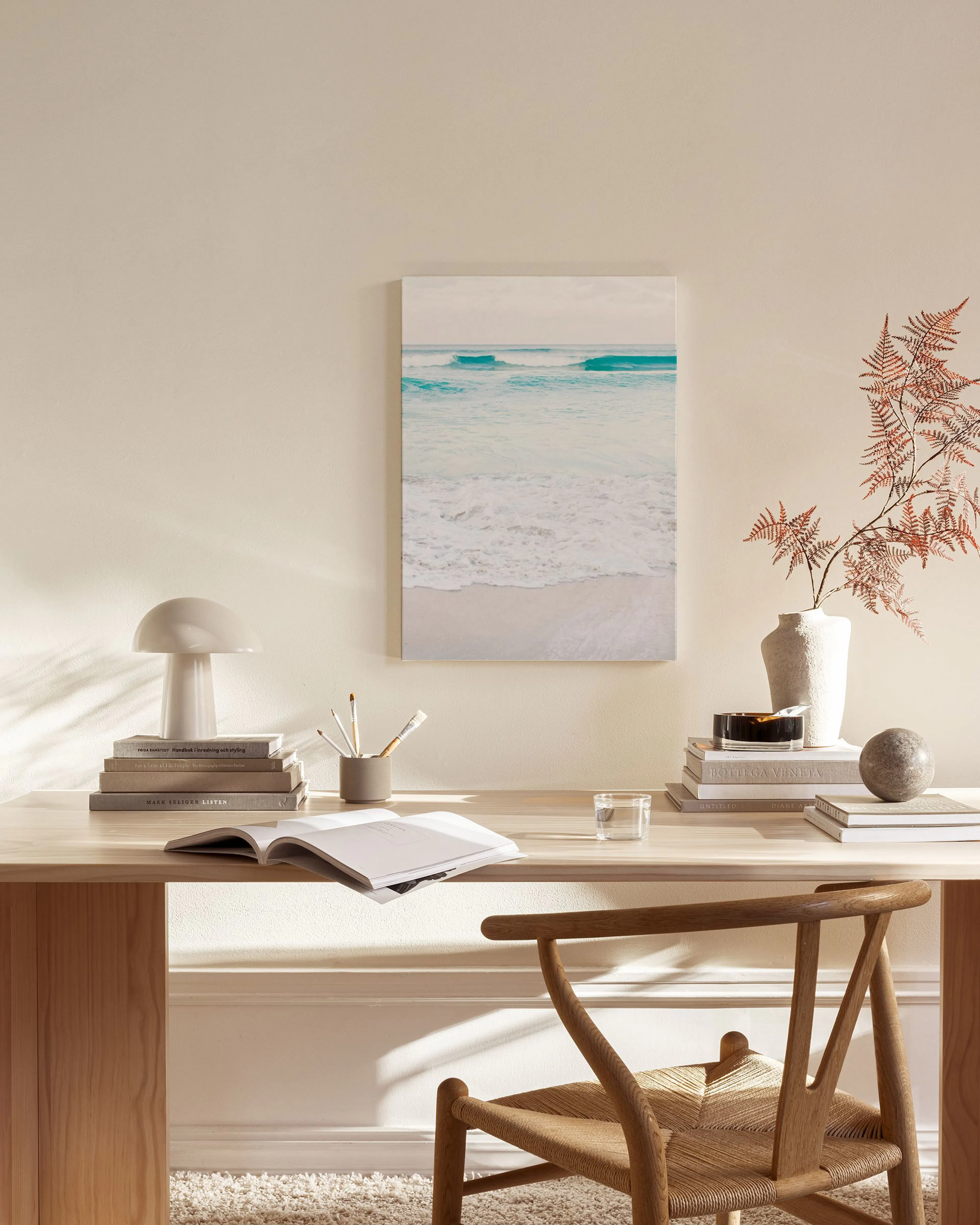A canvas print of gentle blue ocean waves meeting a sandy beach, hanging in a minimalist living room.