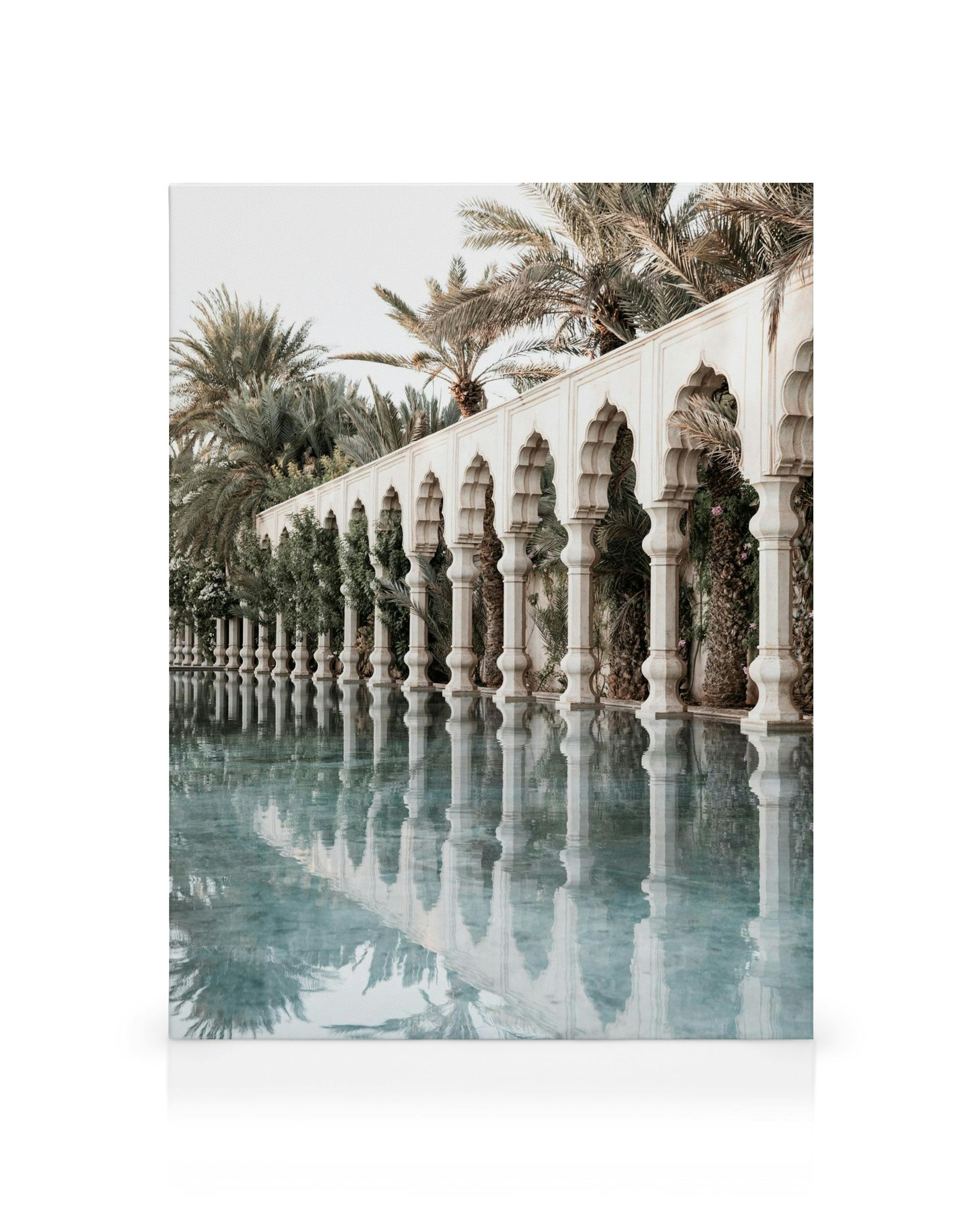 Leinwandbild mit weißen arabischen Bögen, die sich in einem ruhigen Wasserbecken spiegeln, umgeben von Palmen und tropischen Pfl