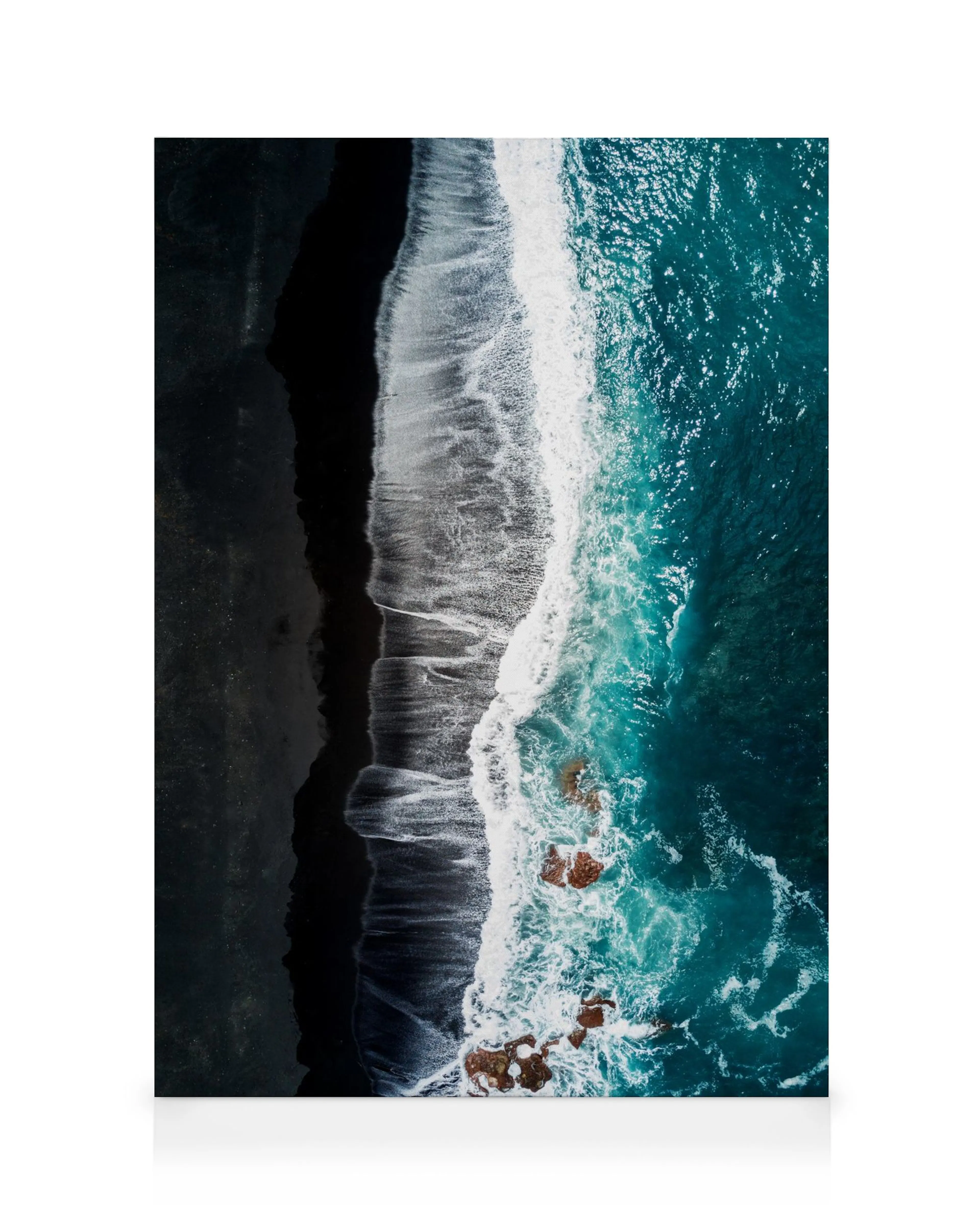 Flygfoto av svart sandstrand med turkosblå vågor som slår mot strandlinjen, exponerade klippor i havet.