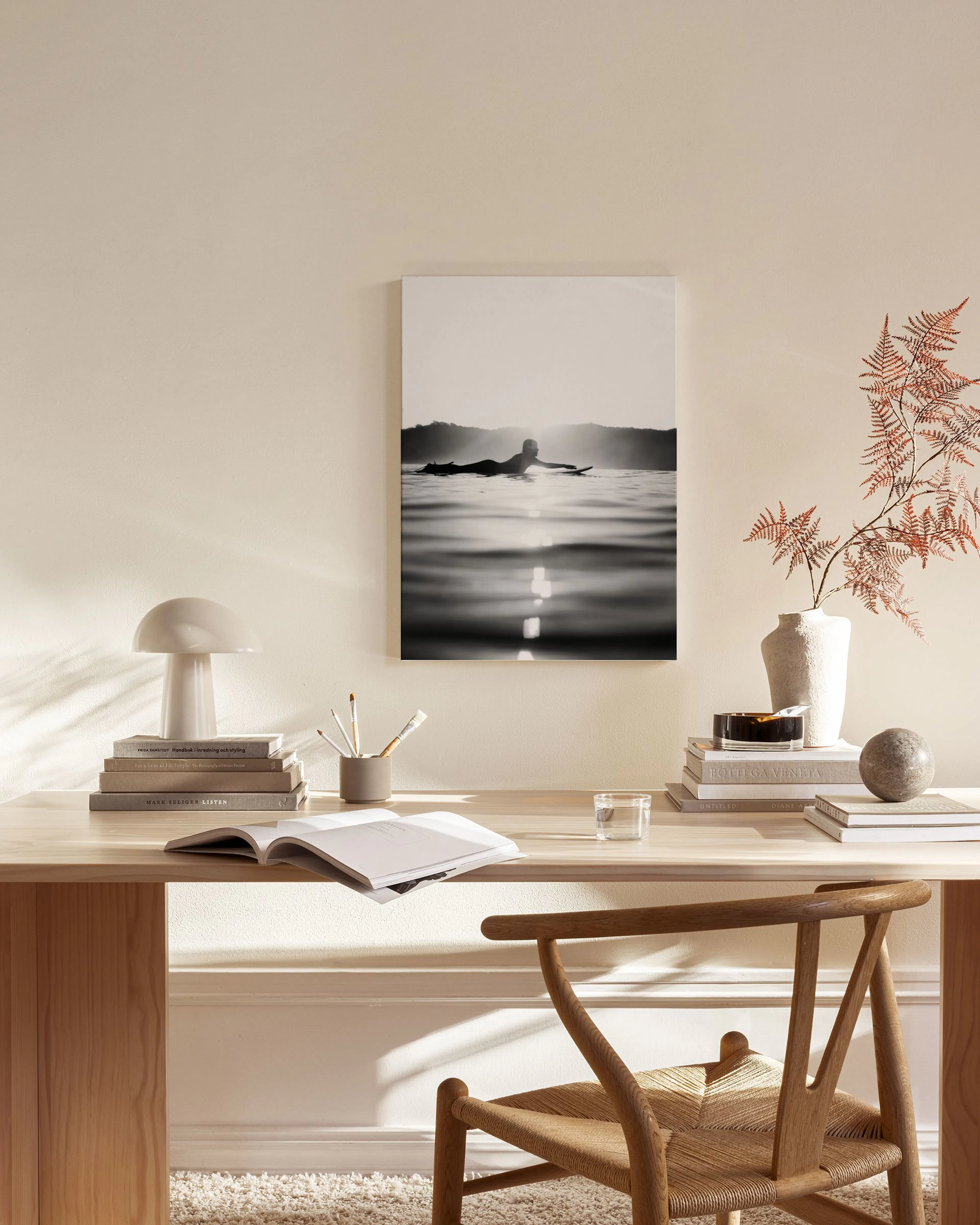 Schwarz-weiß Leinwandbild eines Surfers bei Sonnenuntergang in einem hellen Wohnzimmer mit Holzmöbeln.